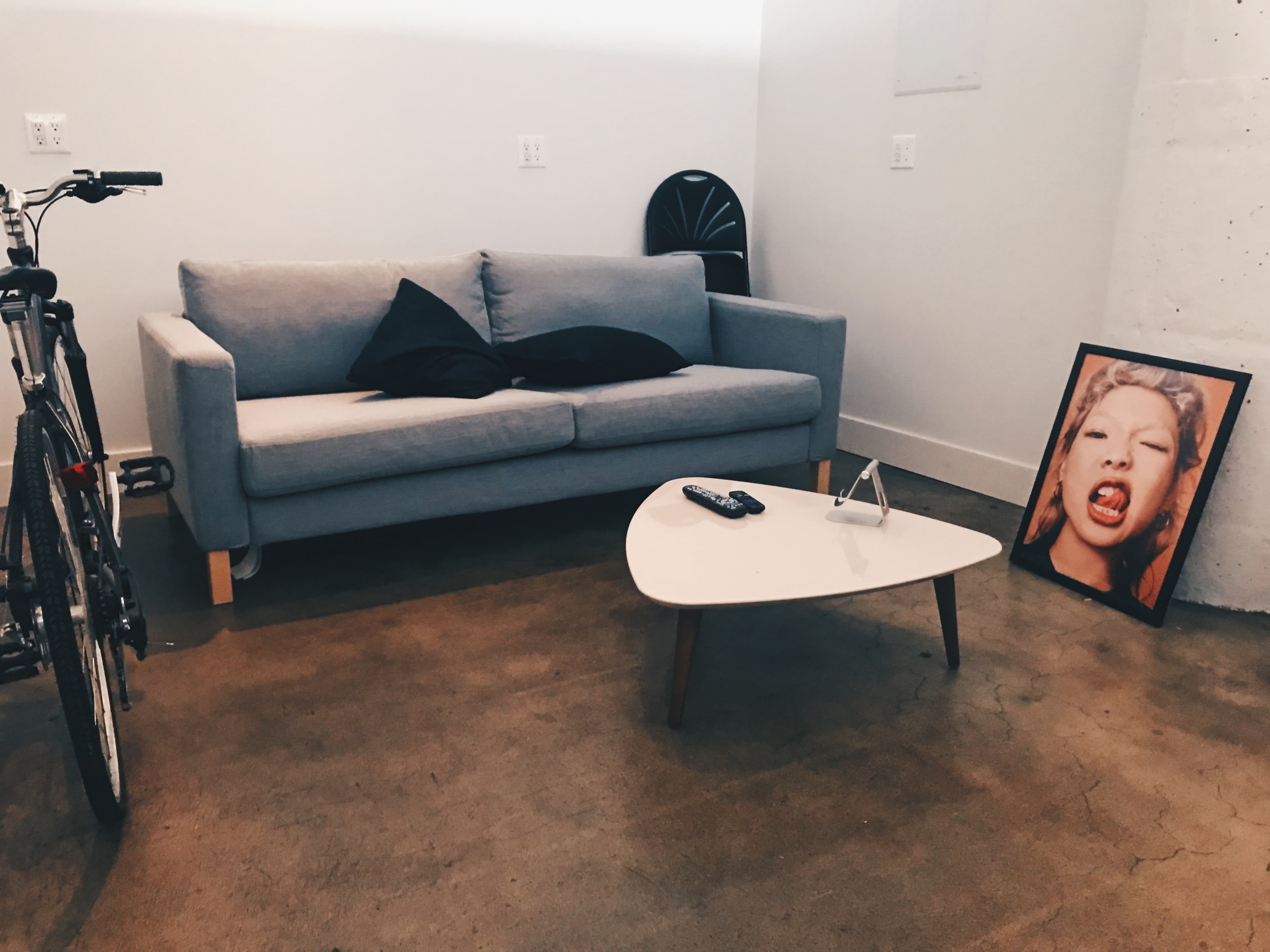 A modern living room with a gray couch, a small white coffee table, a bicycle, and a framed photo of a woman on the floor.