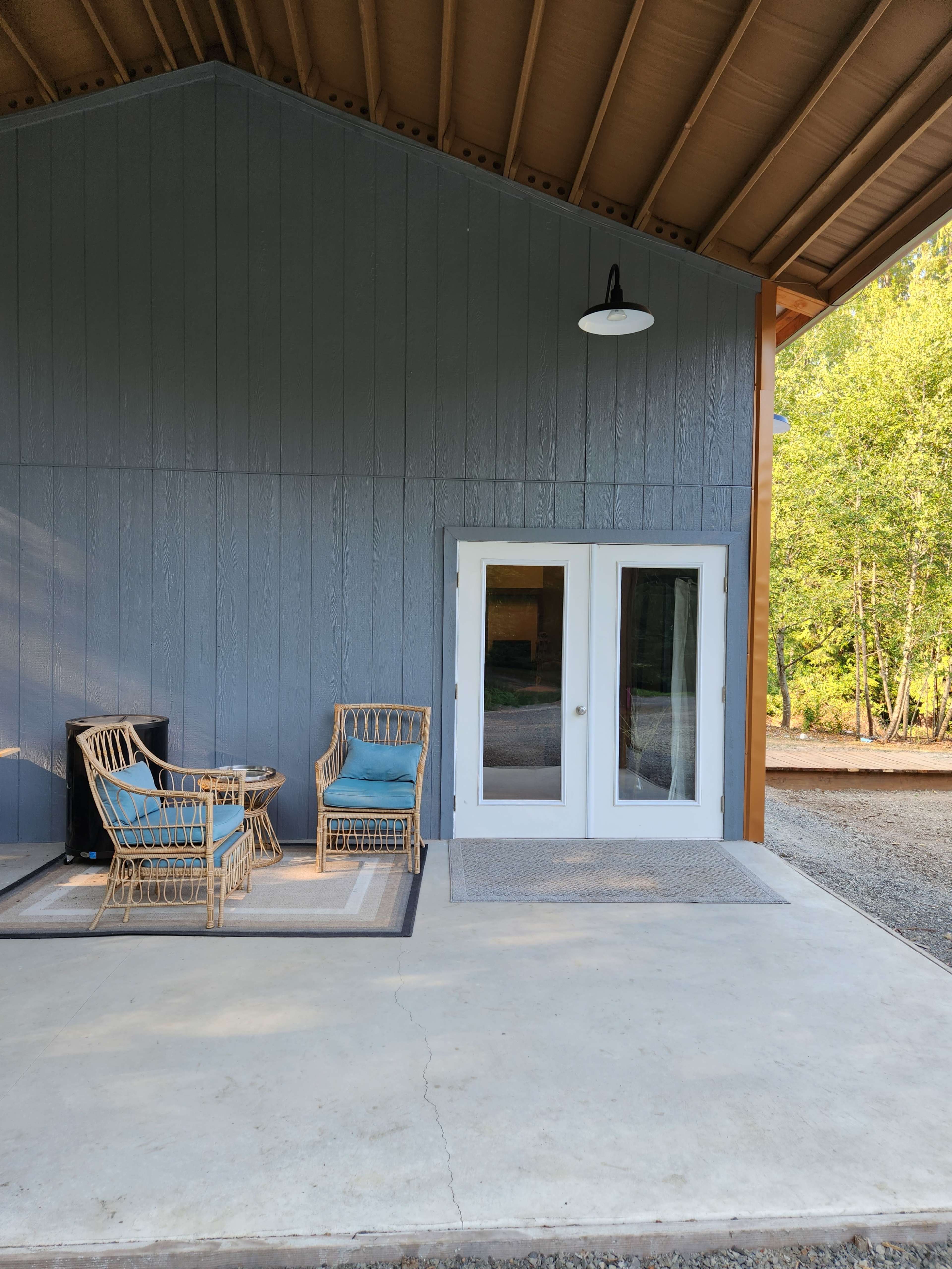 The image shows a porch area with two seating chairs, a small table, and double glass doors leading into a building.