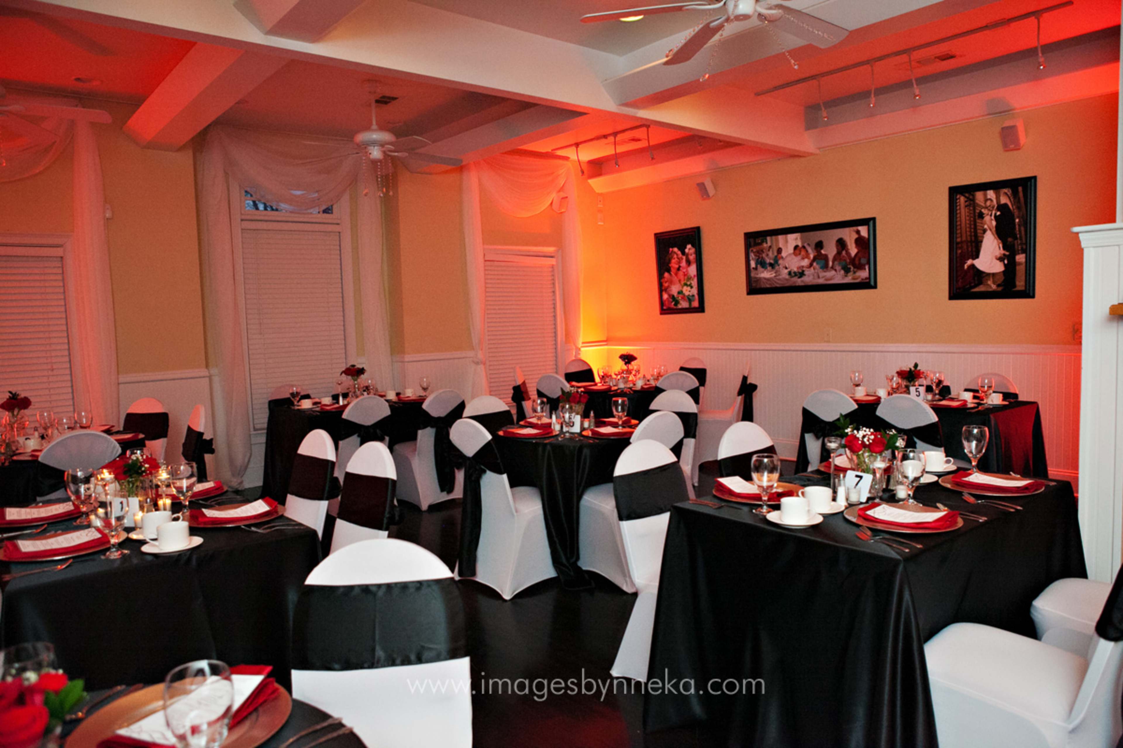 A dining room is set with black and white tablecloths, neatly arranged tableware, and decorative floral centerpieces under warm lighting.