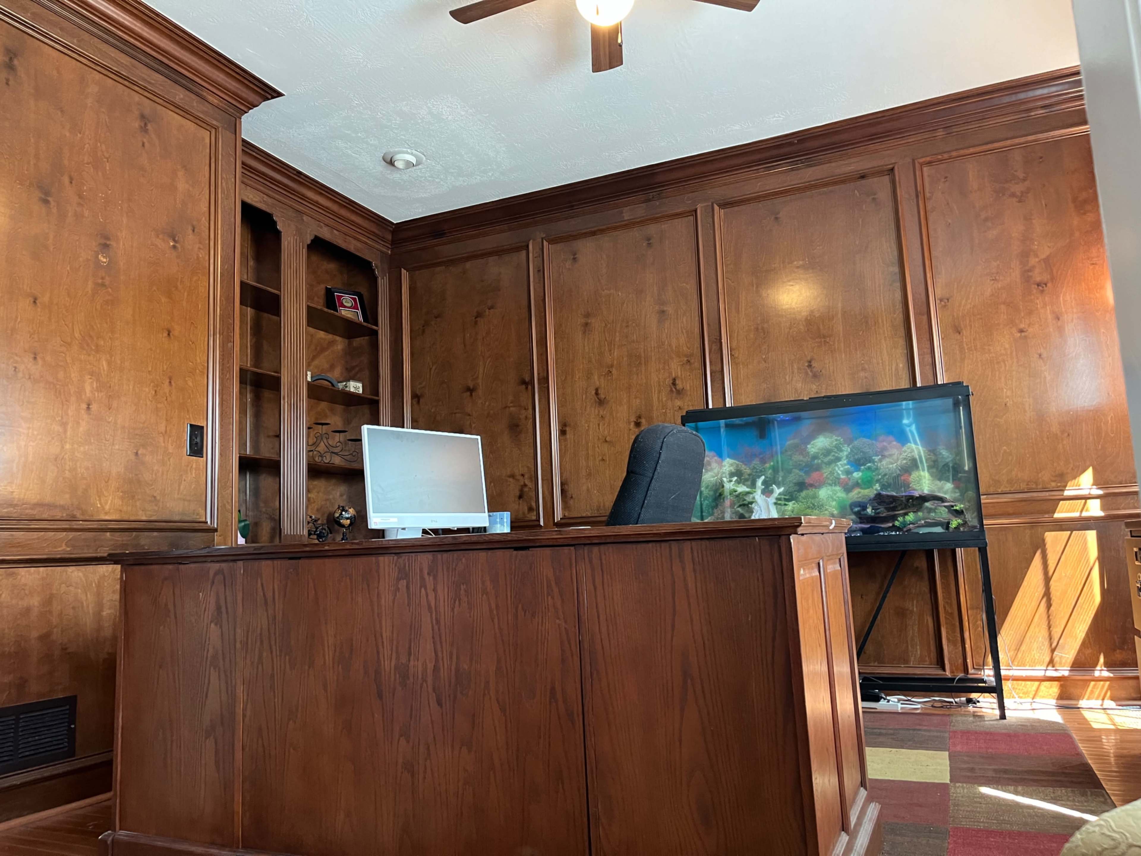 A wooden office with a large desk, a computer monitor, and an aquarium in one corner.