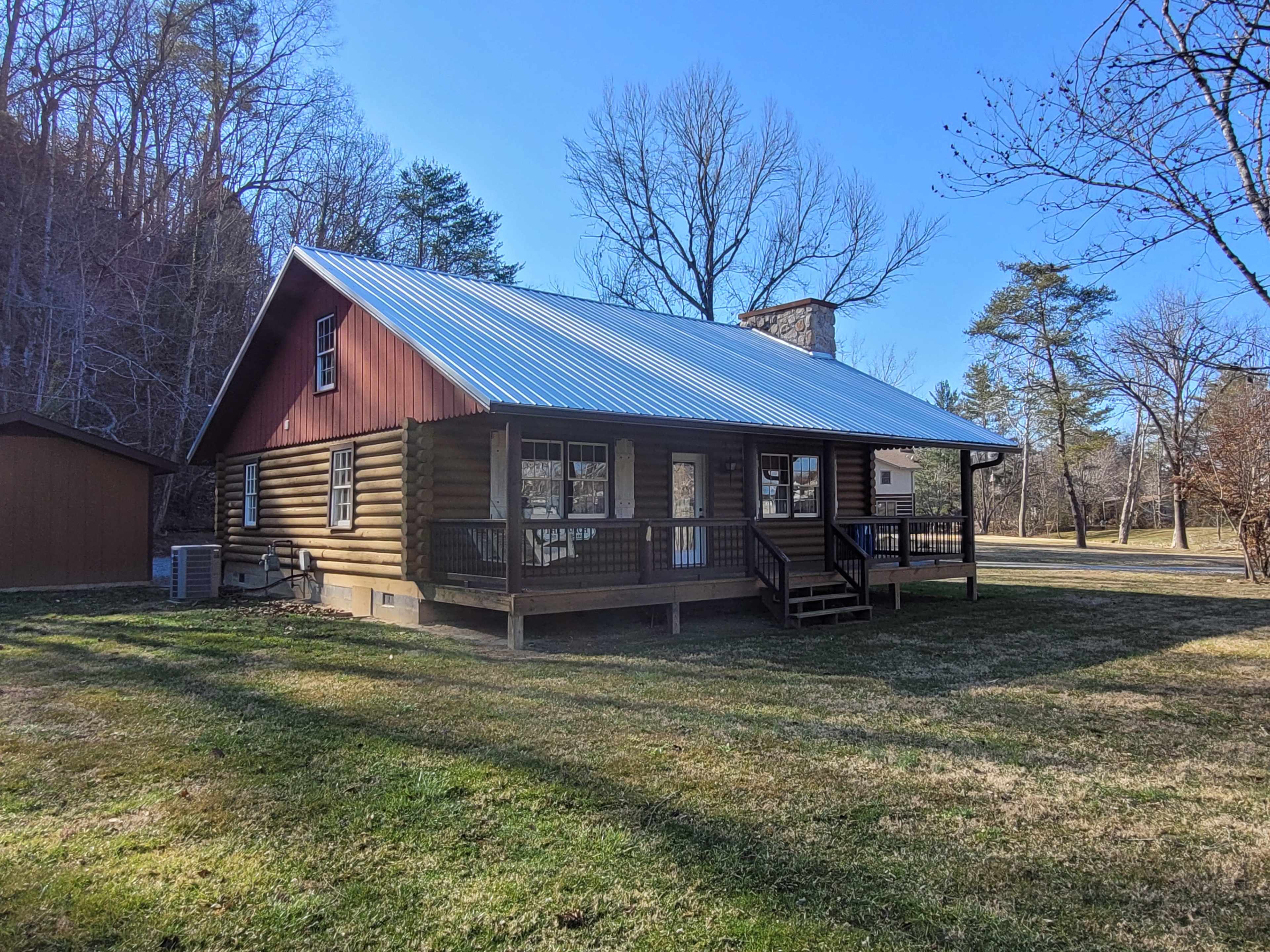 A log cabin with a metal roof is situated in a grassy area surrounded by trees.