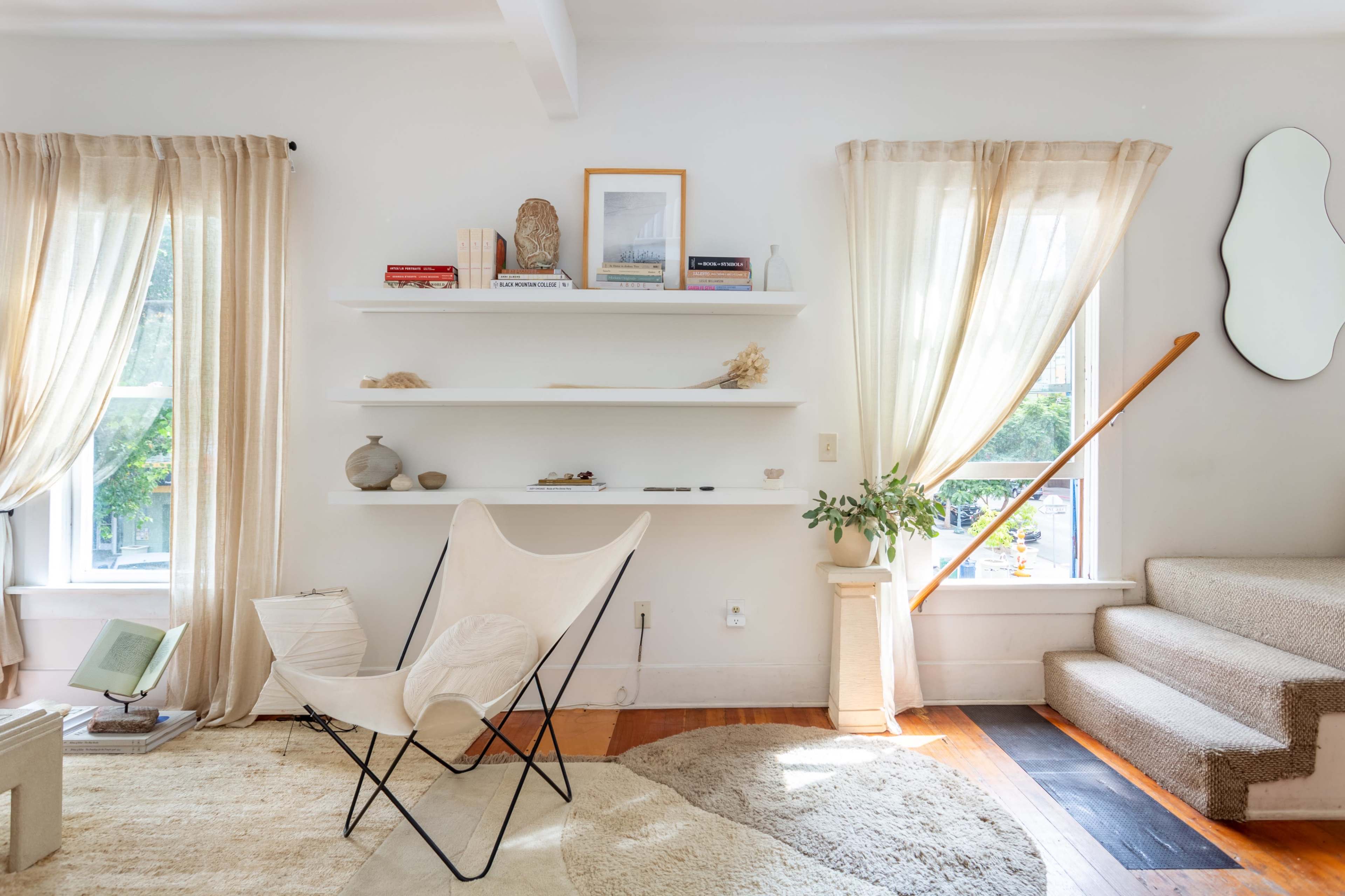 A bright living room featuring a butterfly chair, shelves with decorative items, and steps leading to an upper level.
