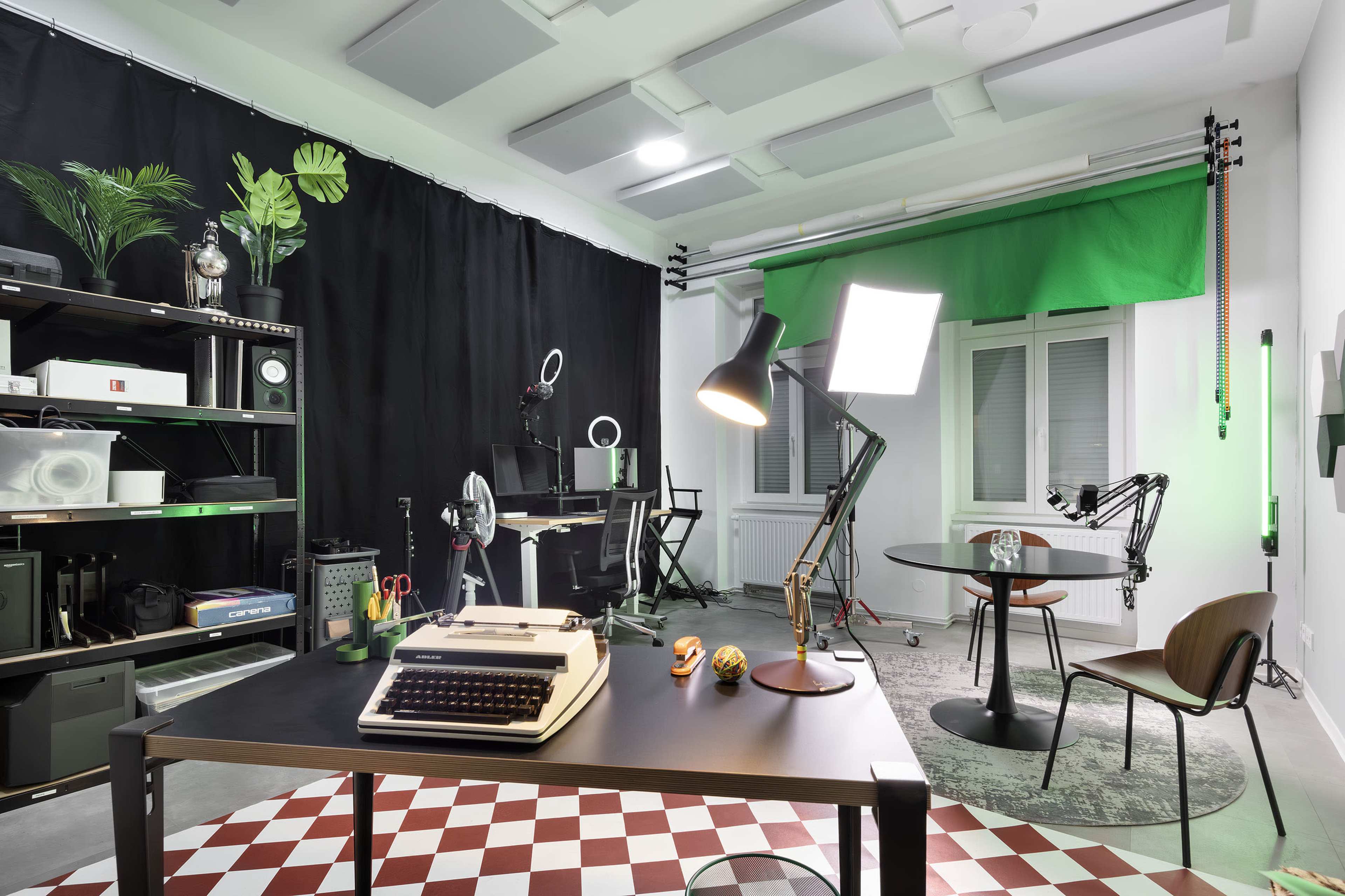 A modern workspace featuring a vintage typewriter on a table, professional lighting equipment, and a green screen in a well-organized studio environment.