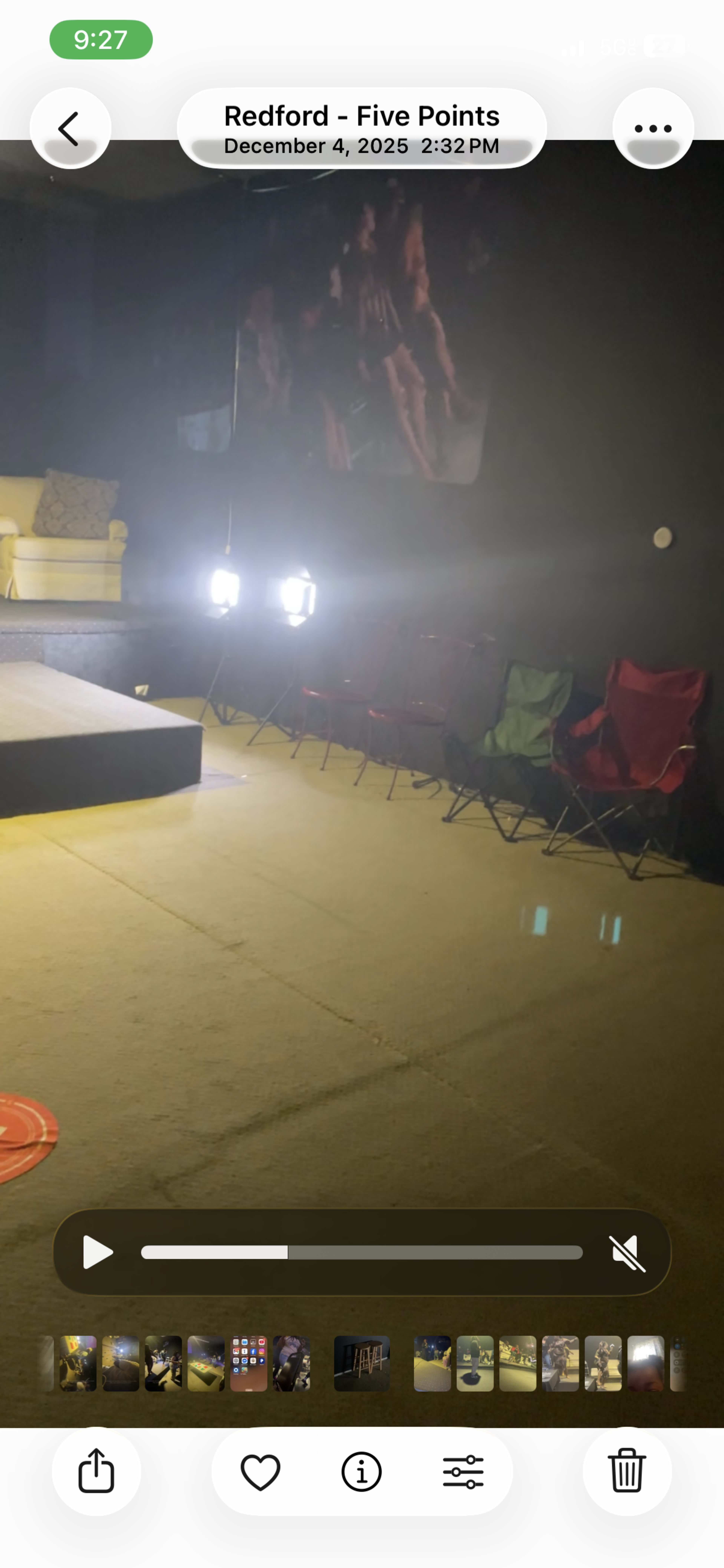 The image shows a dimly lit indoor space featuring a performance stage with chairs arranged in front and a large screen partially visible on the wall.