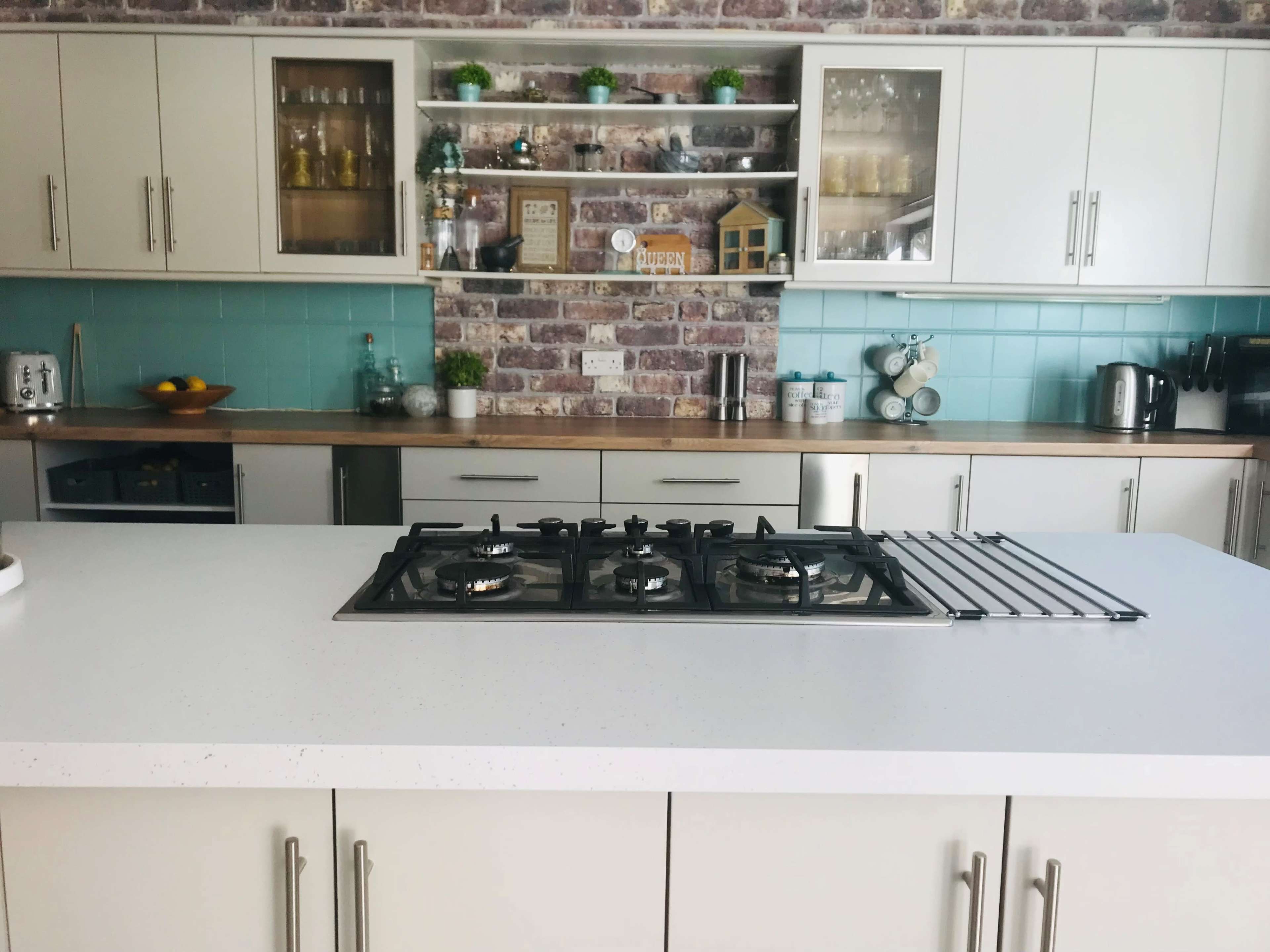 A modern kitchen with white cabinets, a central gas cooktop, and a brick accent wall.