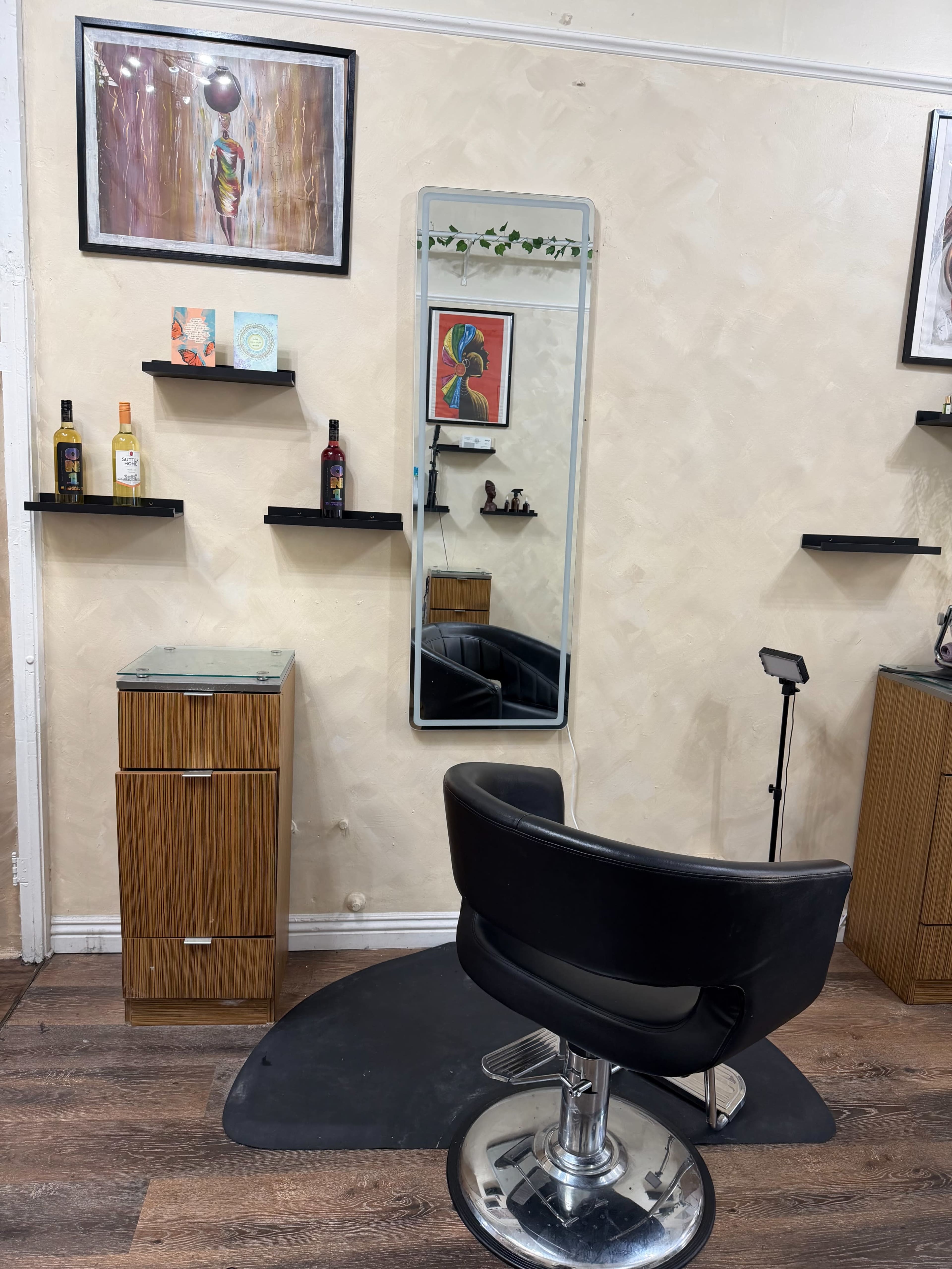 The image shows a hair salon interior featuring a black styling chair, a tall mirror, and shelves displaying various hair products against a light-colored wall.