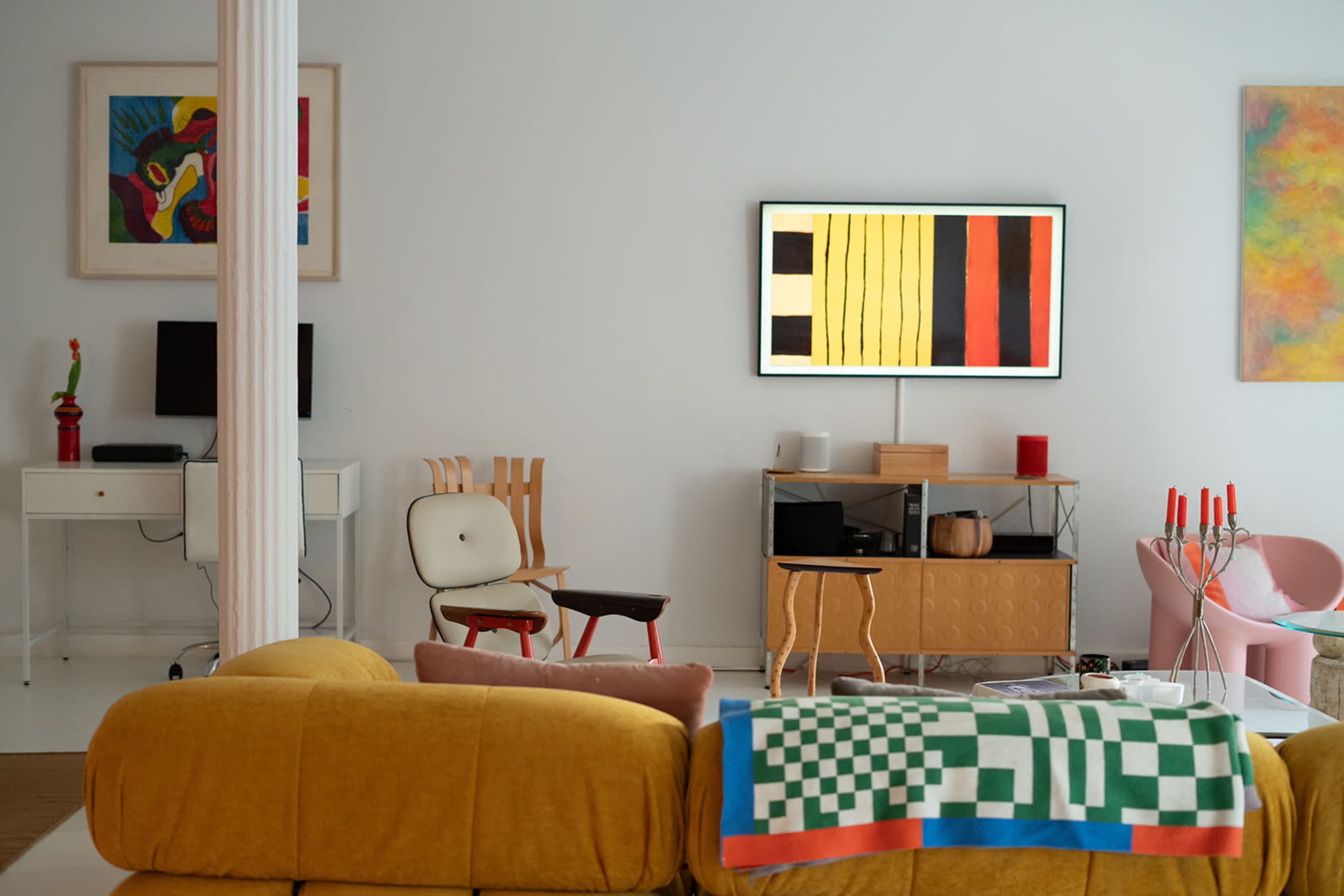 A modern living room features colorful artwork, contemporary furniture, and a television mounted on a white wall.