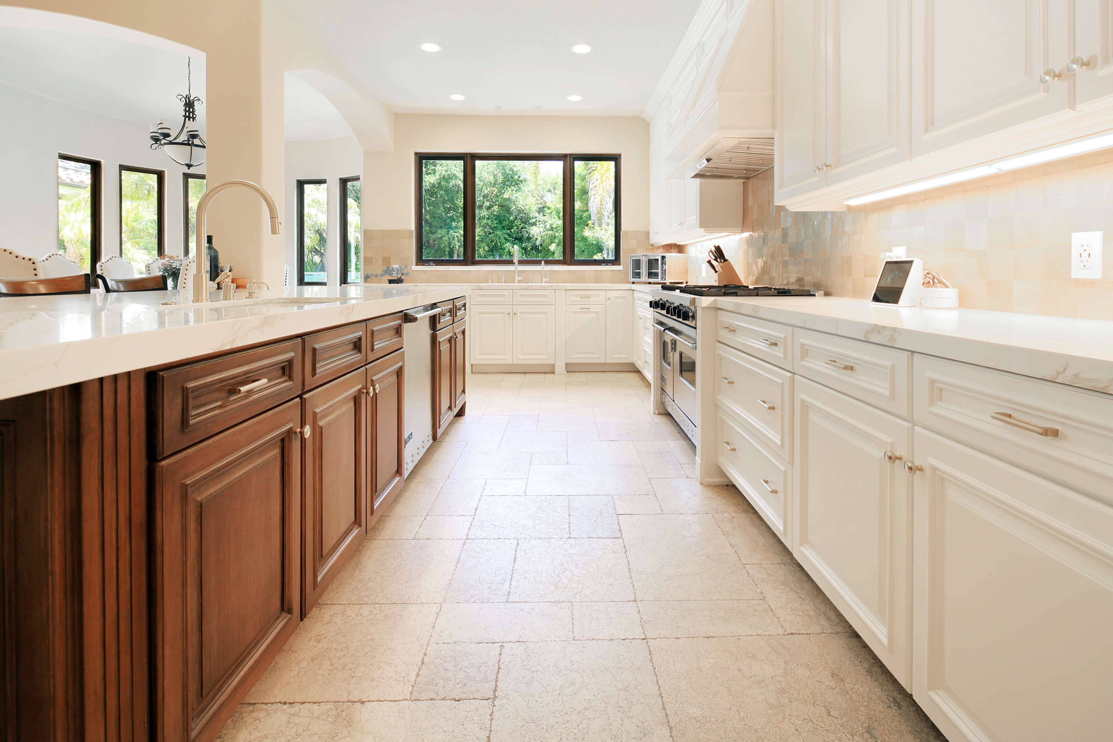 A spacious kitchen features wooden and white cabinetry, a large island, and windows overlooking greenery.
