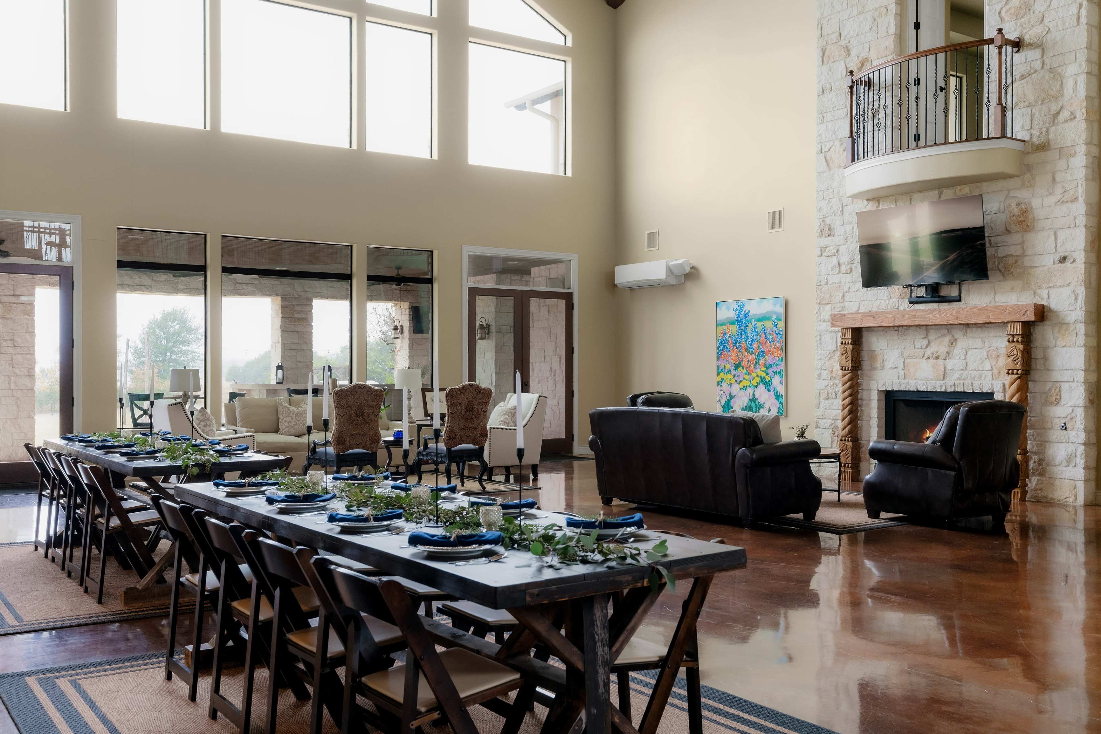 A spacious dining area features a long wooden table set for a meal, with a living space and fireplace visible in the background.