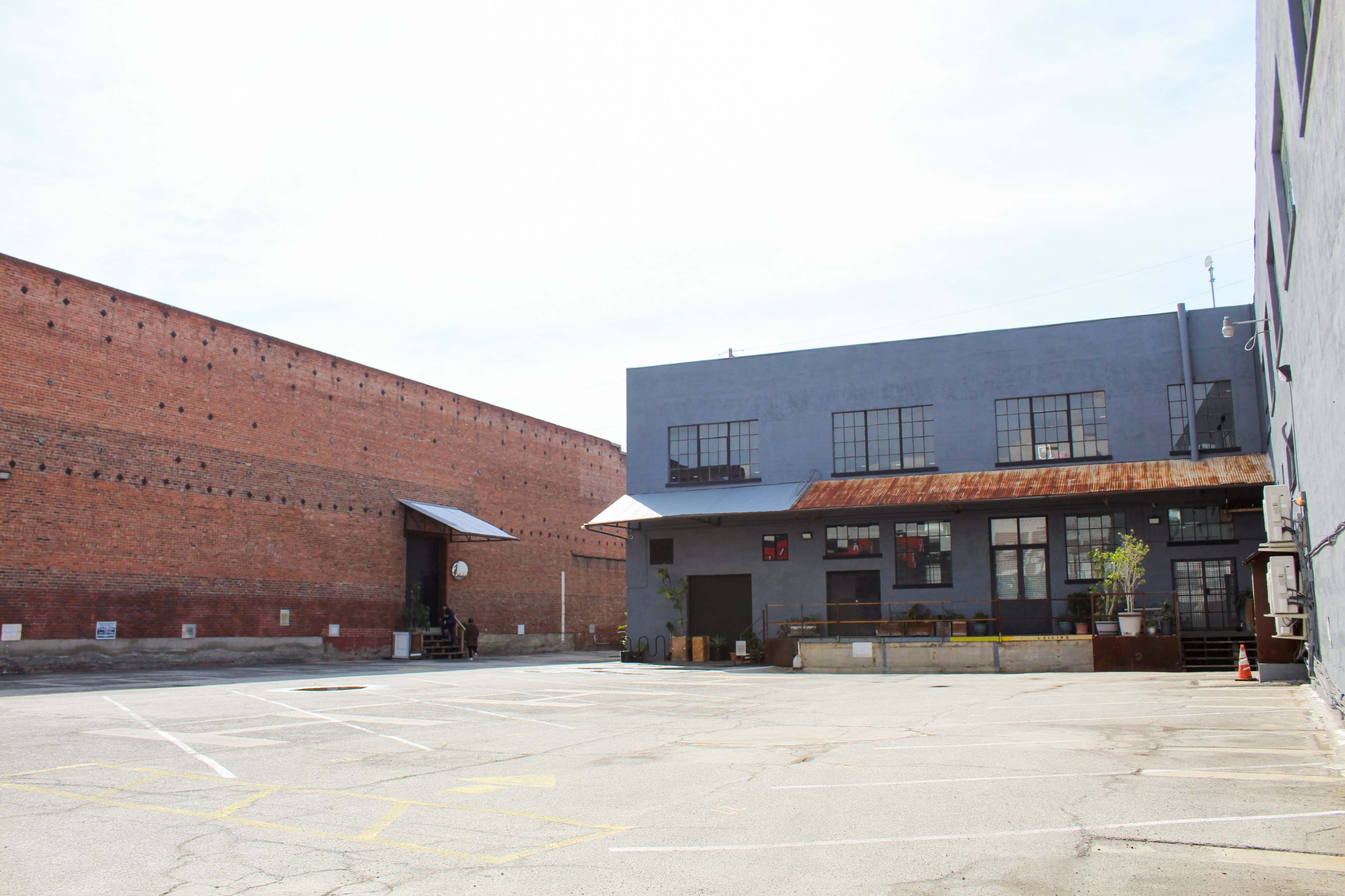 The image shows an empty parking lot next to industrial buildings with a brick wall in the background.