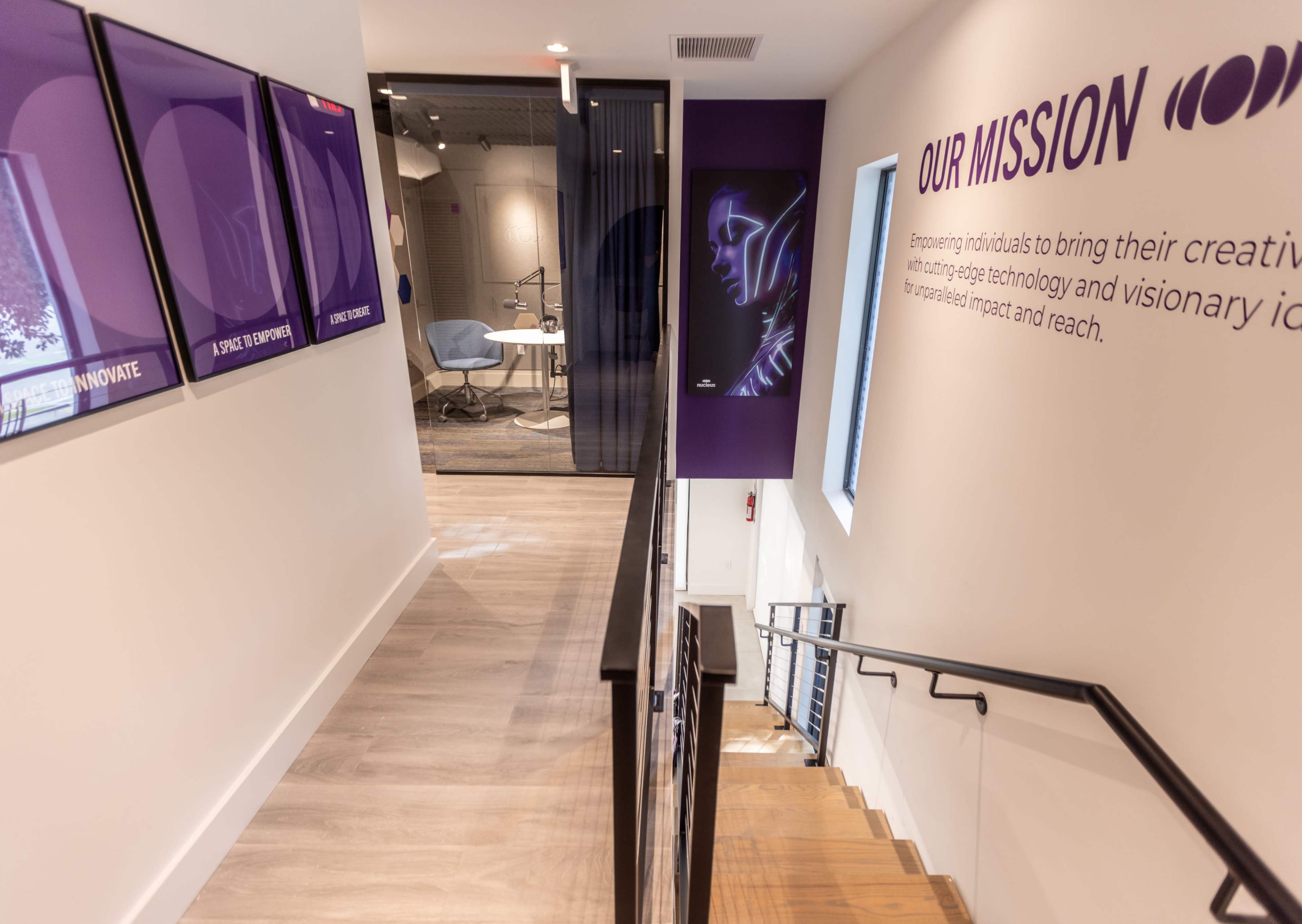 A staircase leads down to a workspace area featuring modern decor and a wall displaying the mission statement.
