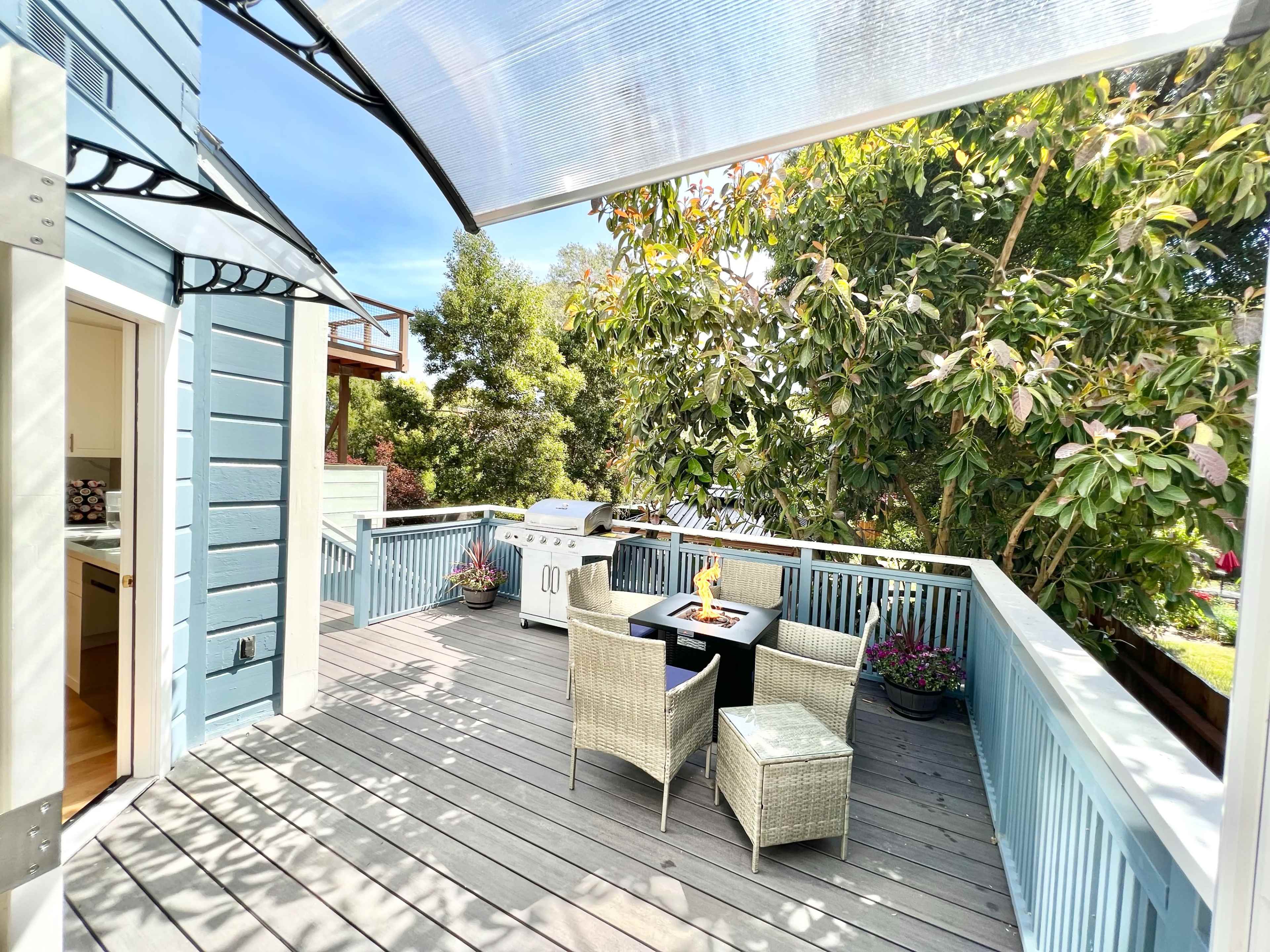 A wooden deck features outdoor furniture and a grill, surrounded by greenery.