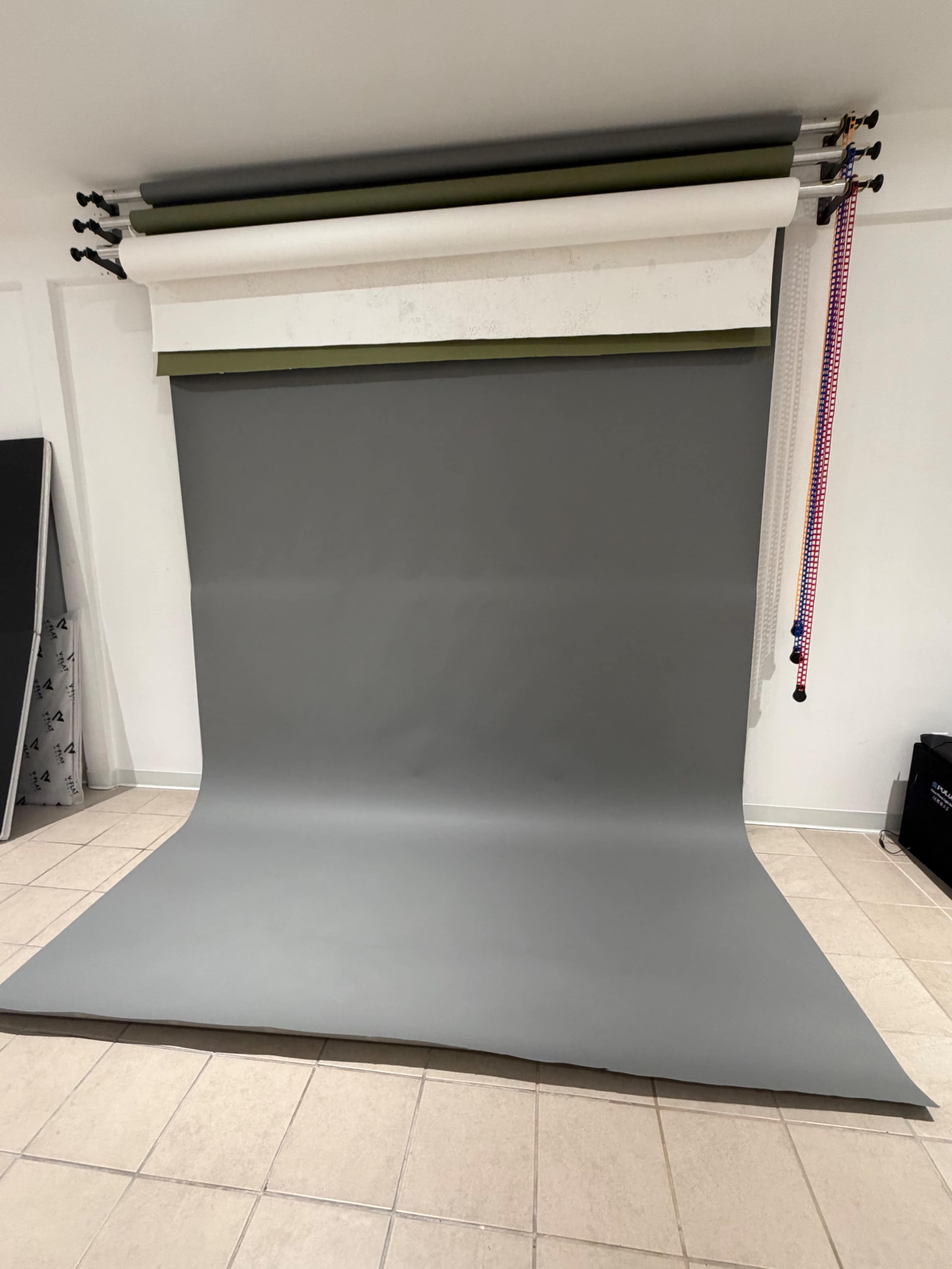 The image shows a photography studio backdrop setup with a gray seamless backdrop installed on a rack, positioned on a tiled floor.