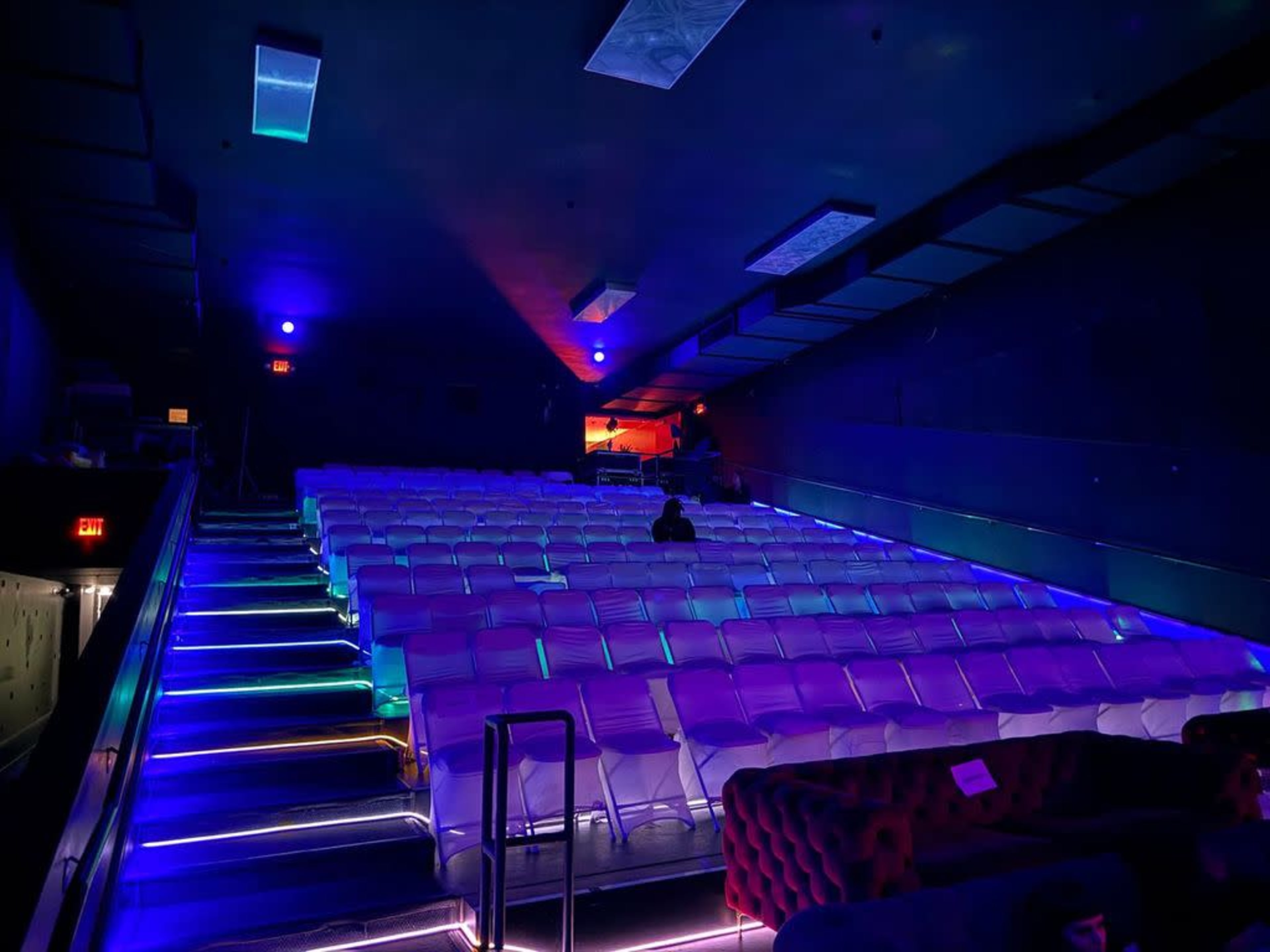 An empty theater filled with rows of white chairs, illuminated by colorful ambient lighting.