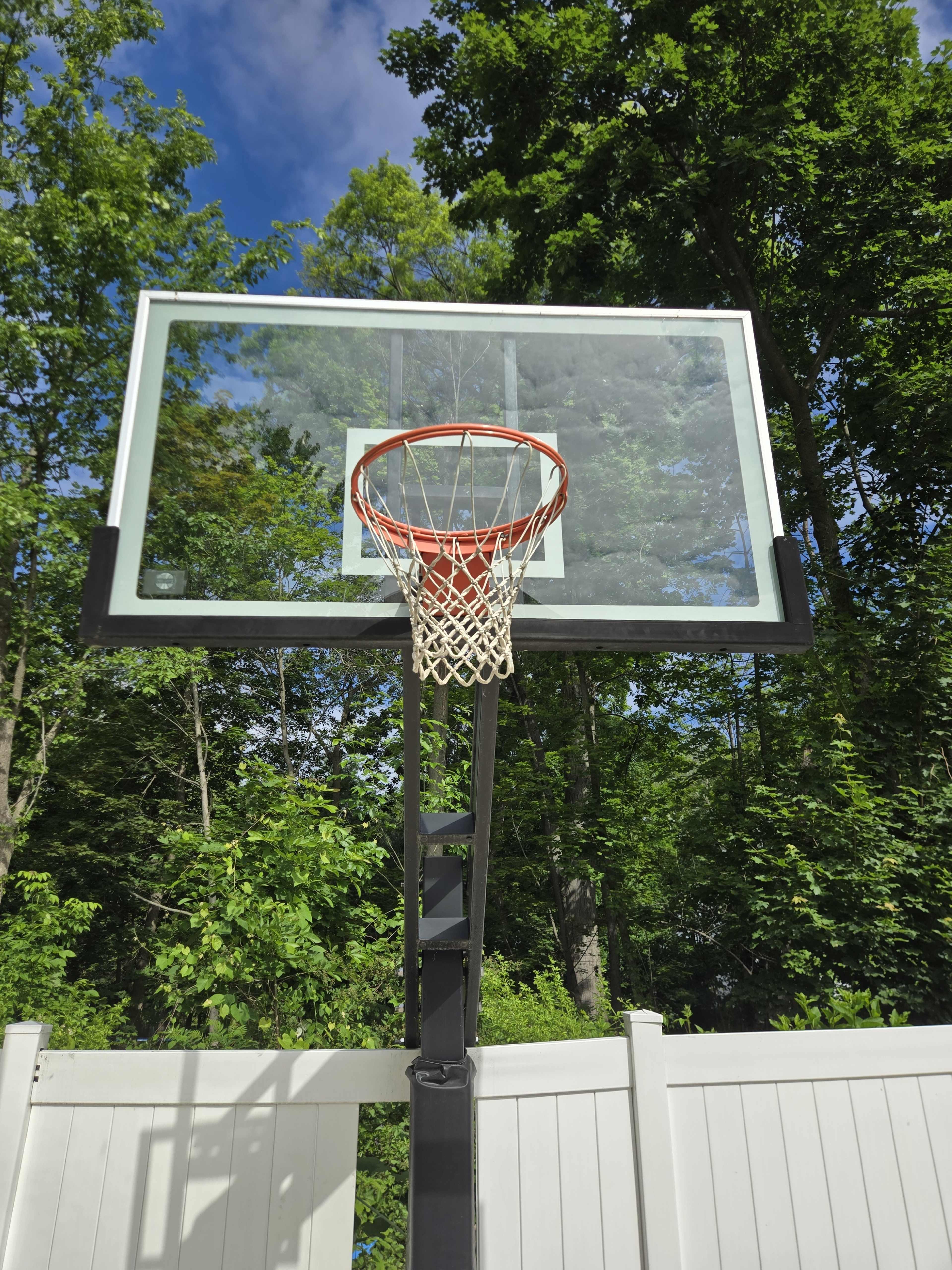 A basketball hoop stands against a backdrop of green trees and blue sky.