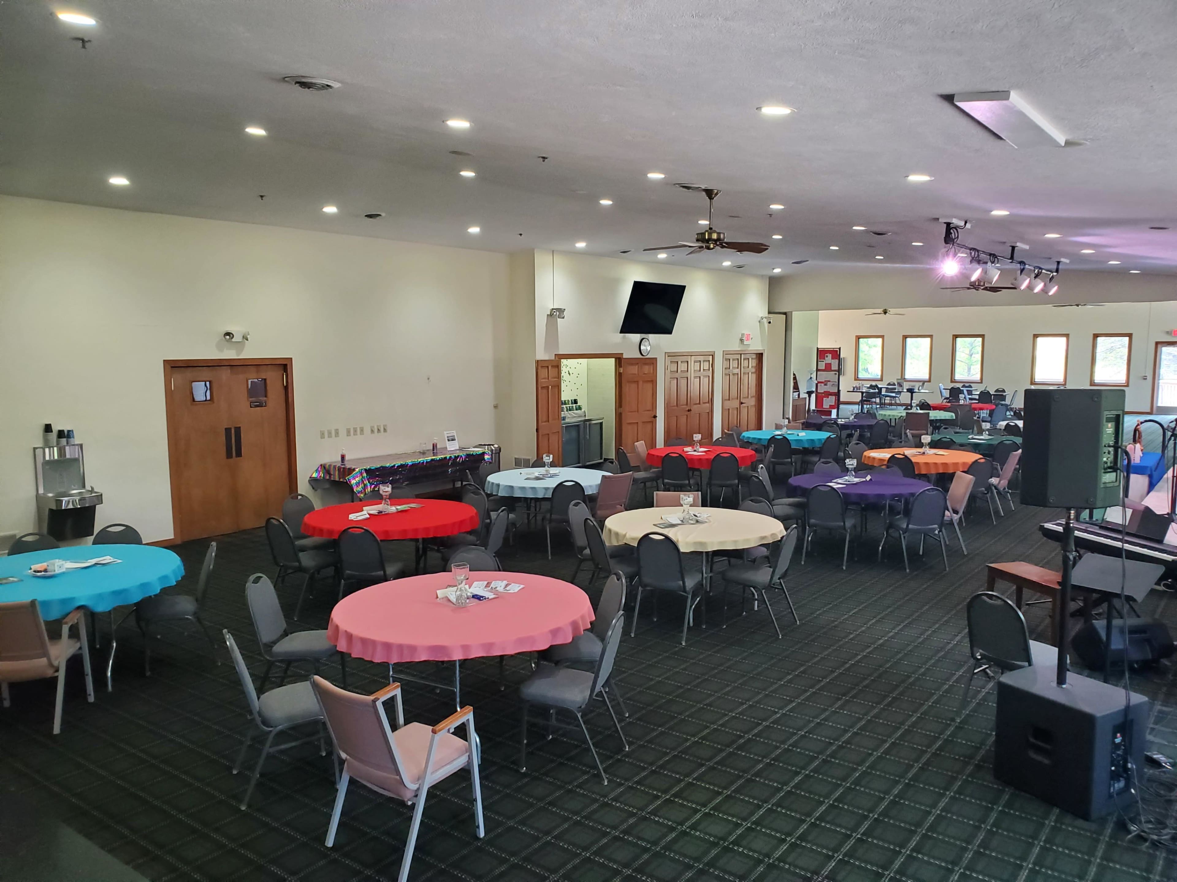 A large event space with several round tables dressed in colorful tablecloths and chairs arranged around them.
