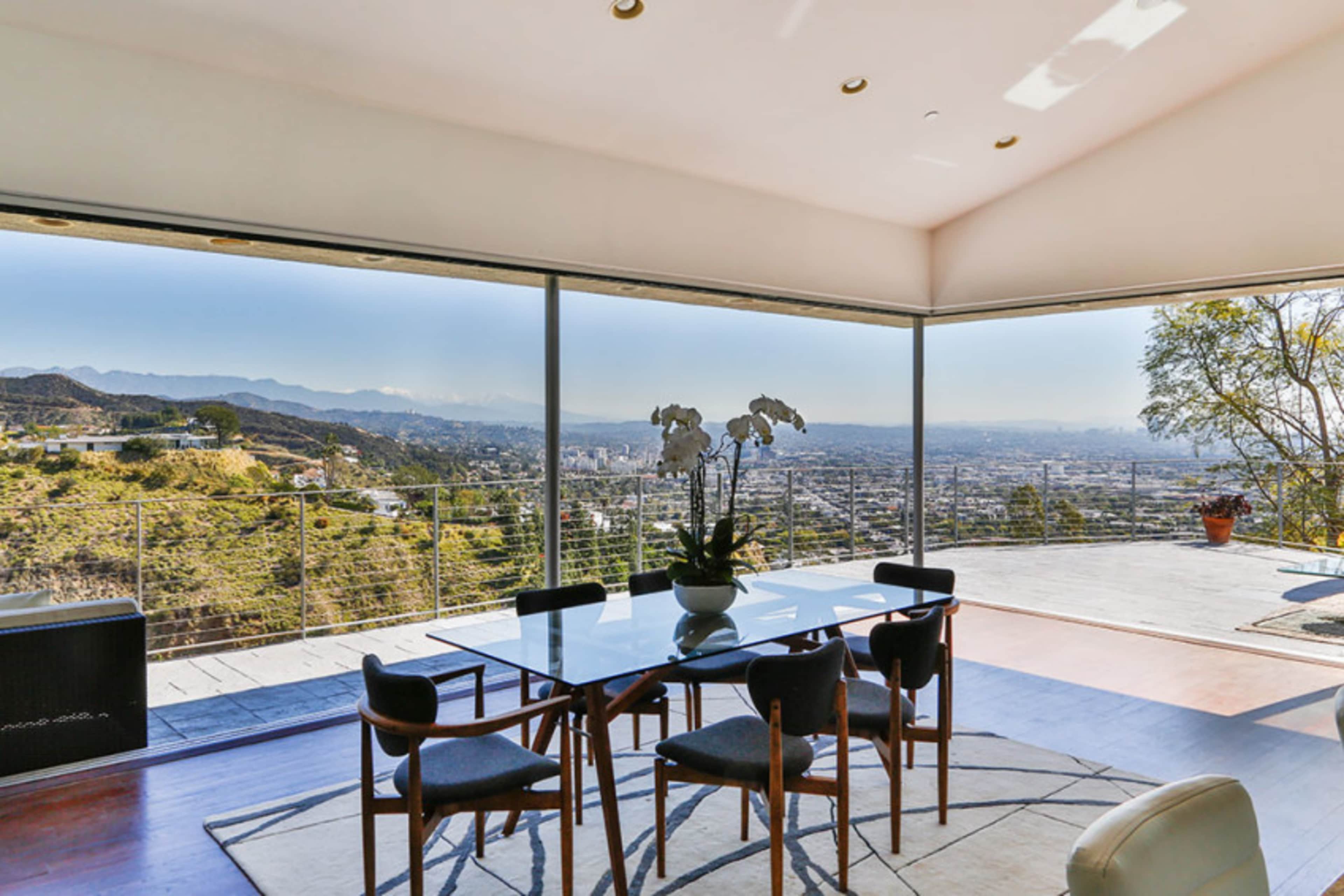 A modern dining area with a glass wall overlooking a mountainous landscape and city skyline.