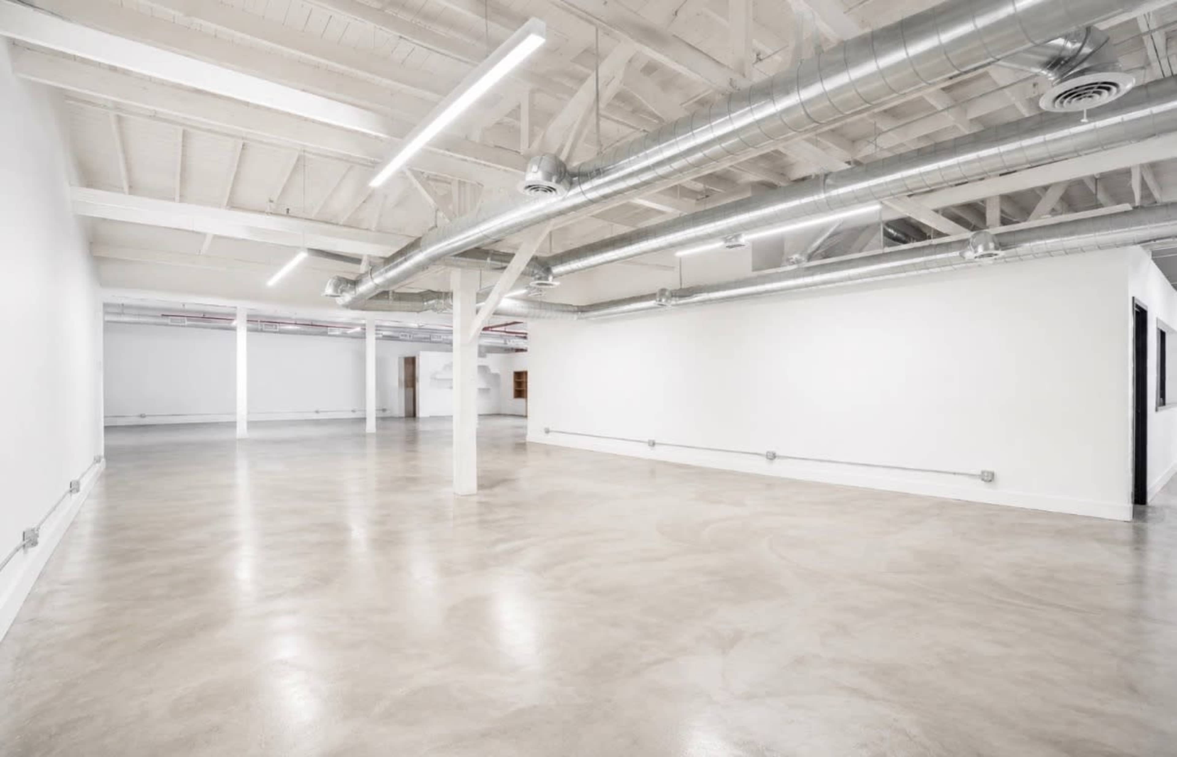 The image shows a spacious, empty interior with polished concrete flooring, white walls, and exposed ductwork along the ceiling.