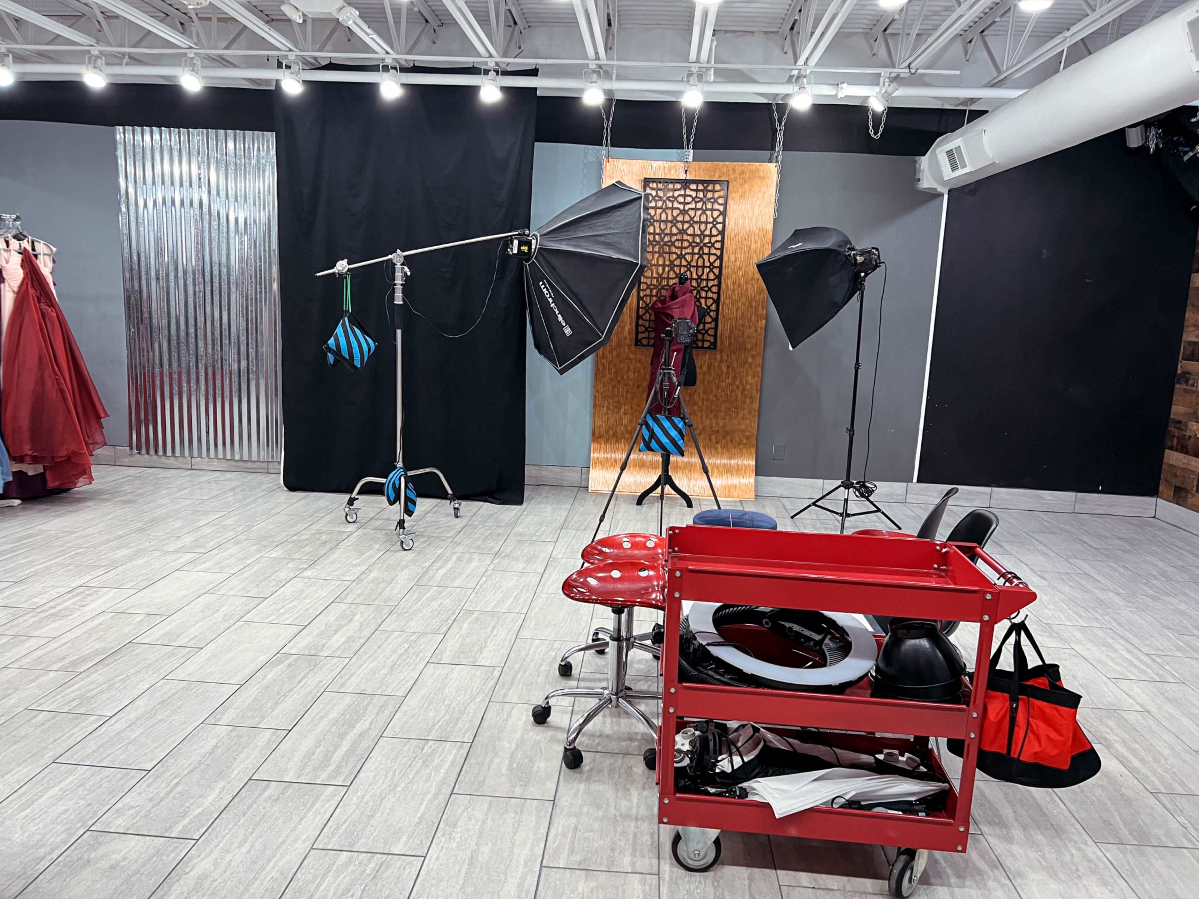 A photography studio setup featuring lighting equipment, a red cart with various items, and a backdrop.