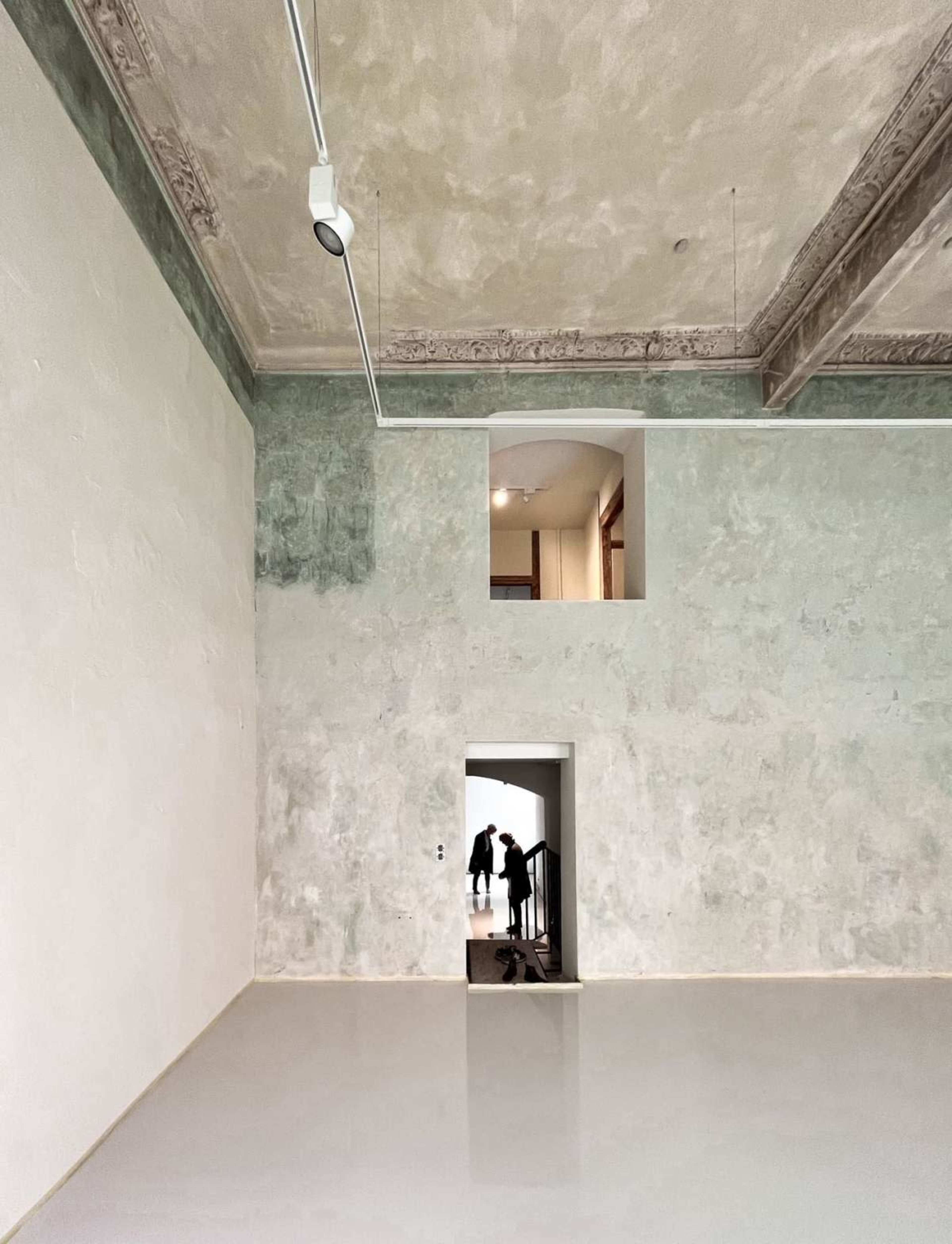 An interior space features a textured wall with a small window and an open doorway leading to a staircase.