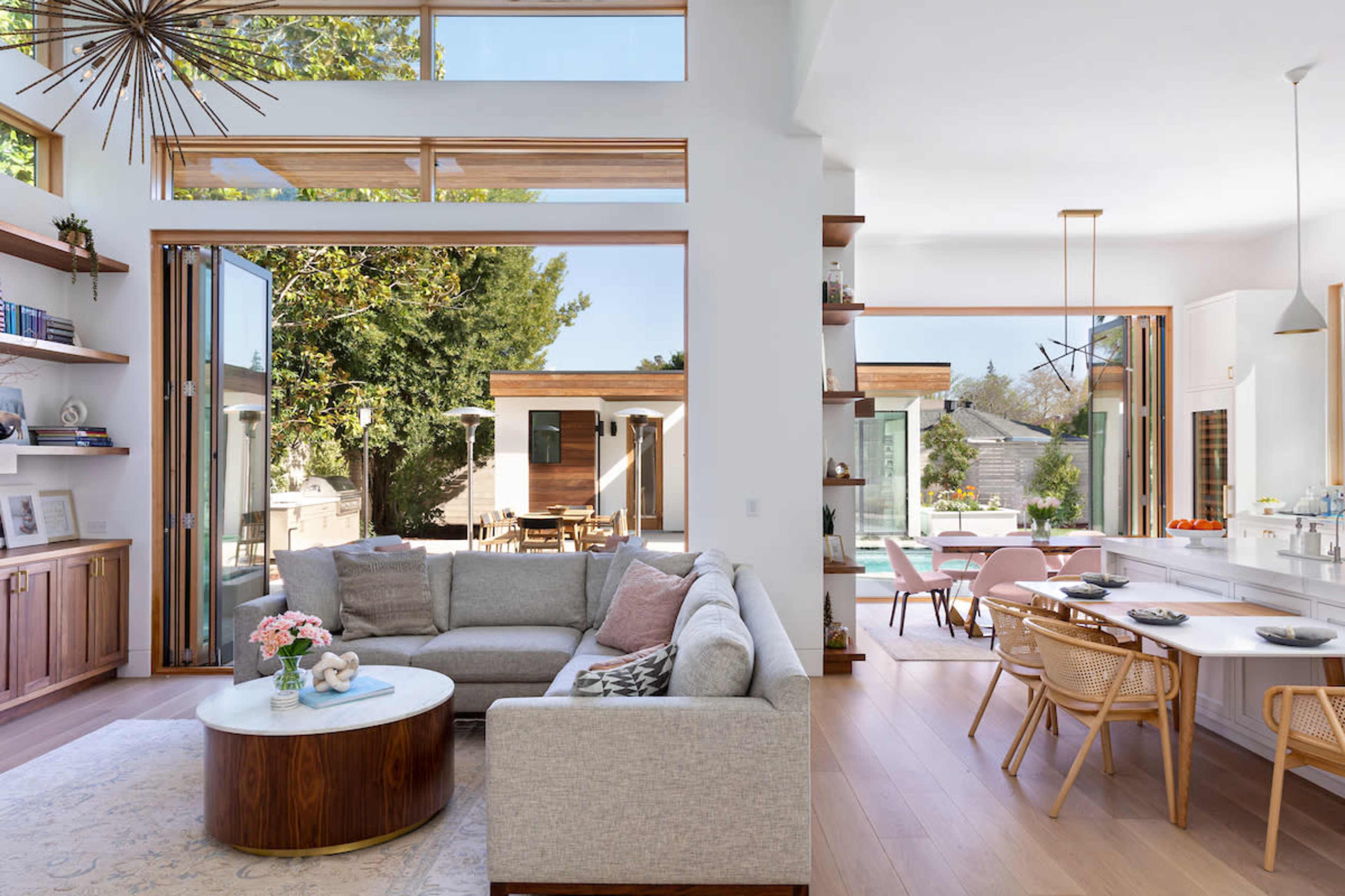 A modern open-concept living space with a light gray sectional sofa, a round coffee table, and large glass doors leading to an outdoor area.