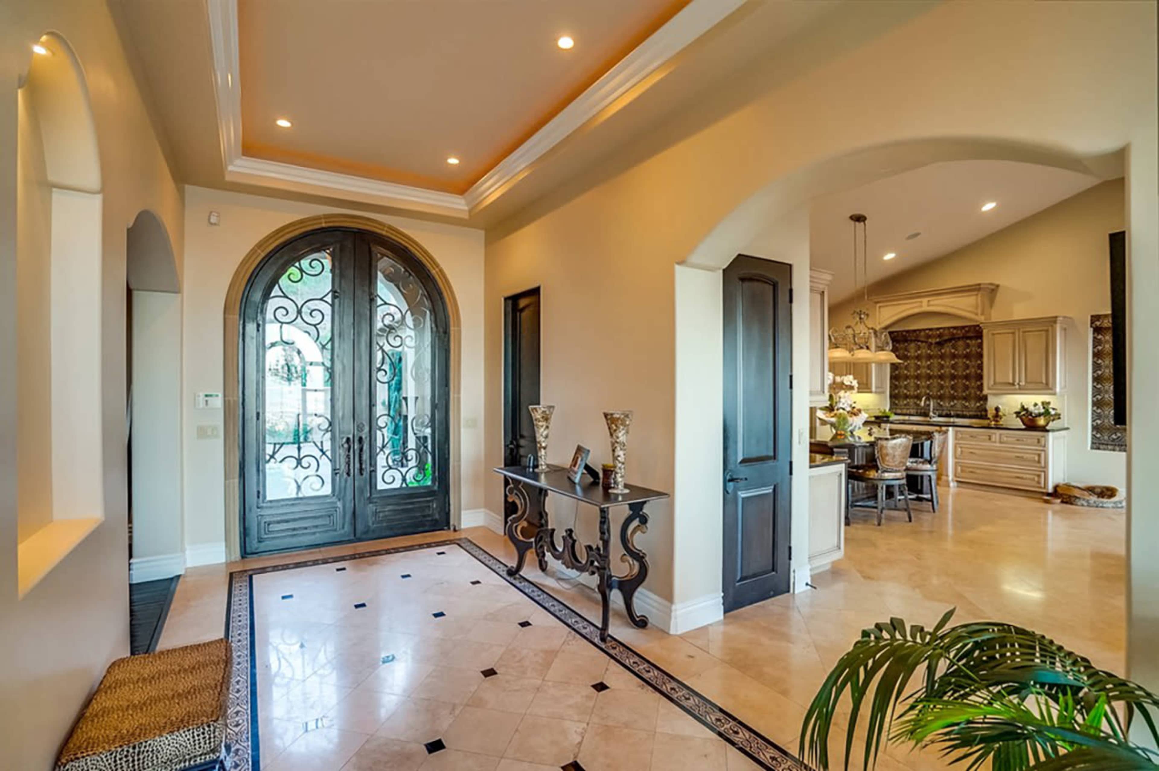 A spacious entryway with a large arched door, decorative flooring, and a view of a kitchen through an open archway.