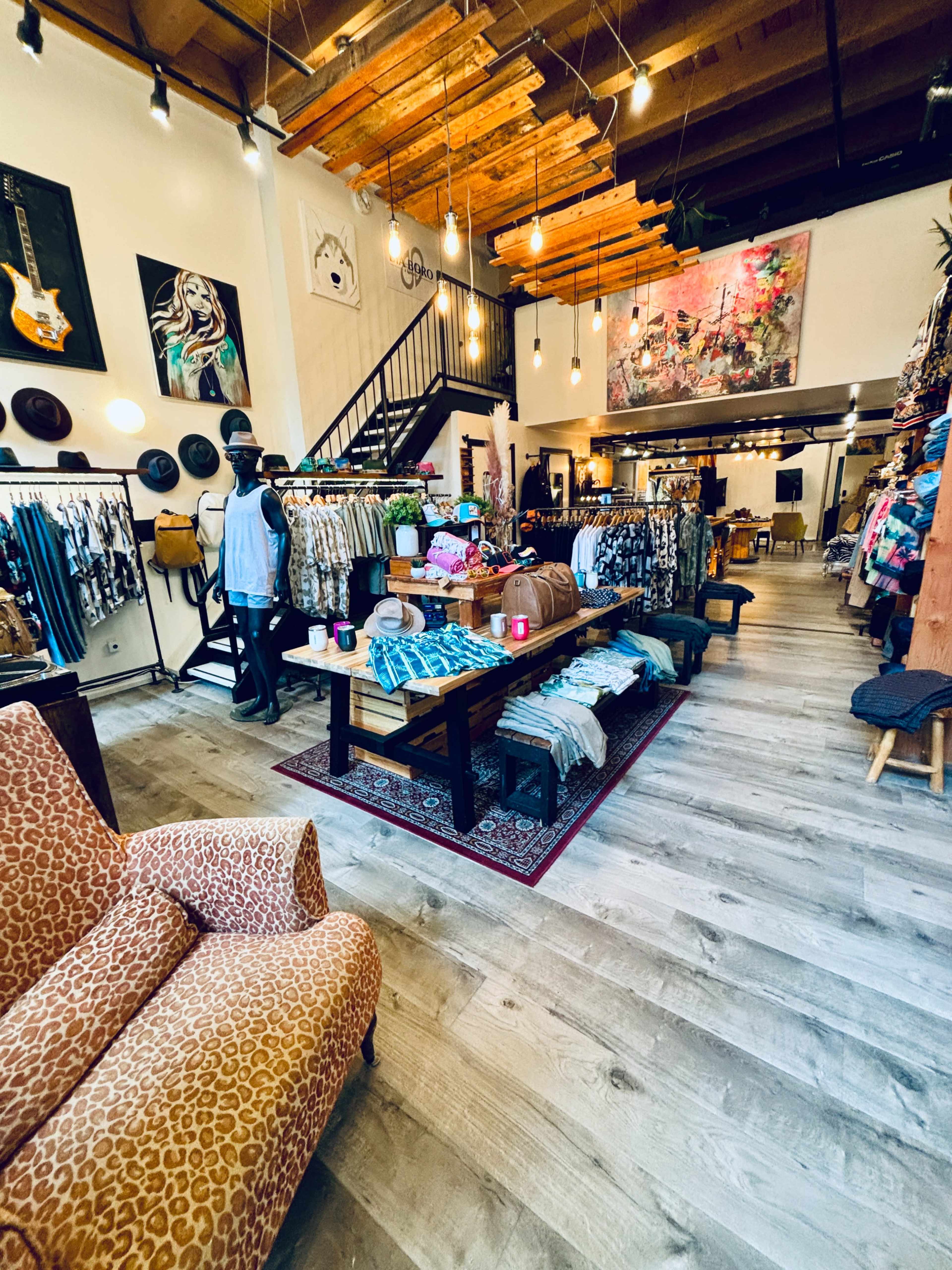 A clothing boutique interior featuring racks of apparel, a patterned rug, and a cozy seating area with a patterned chair.