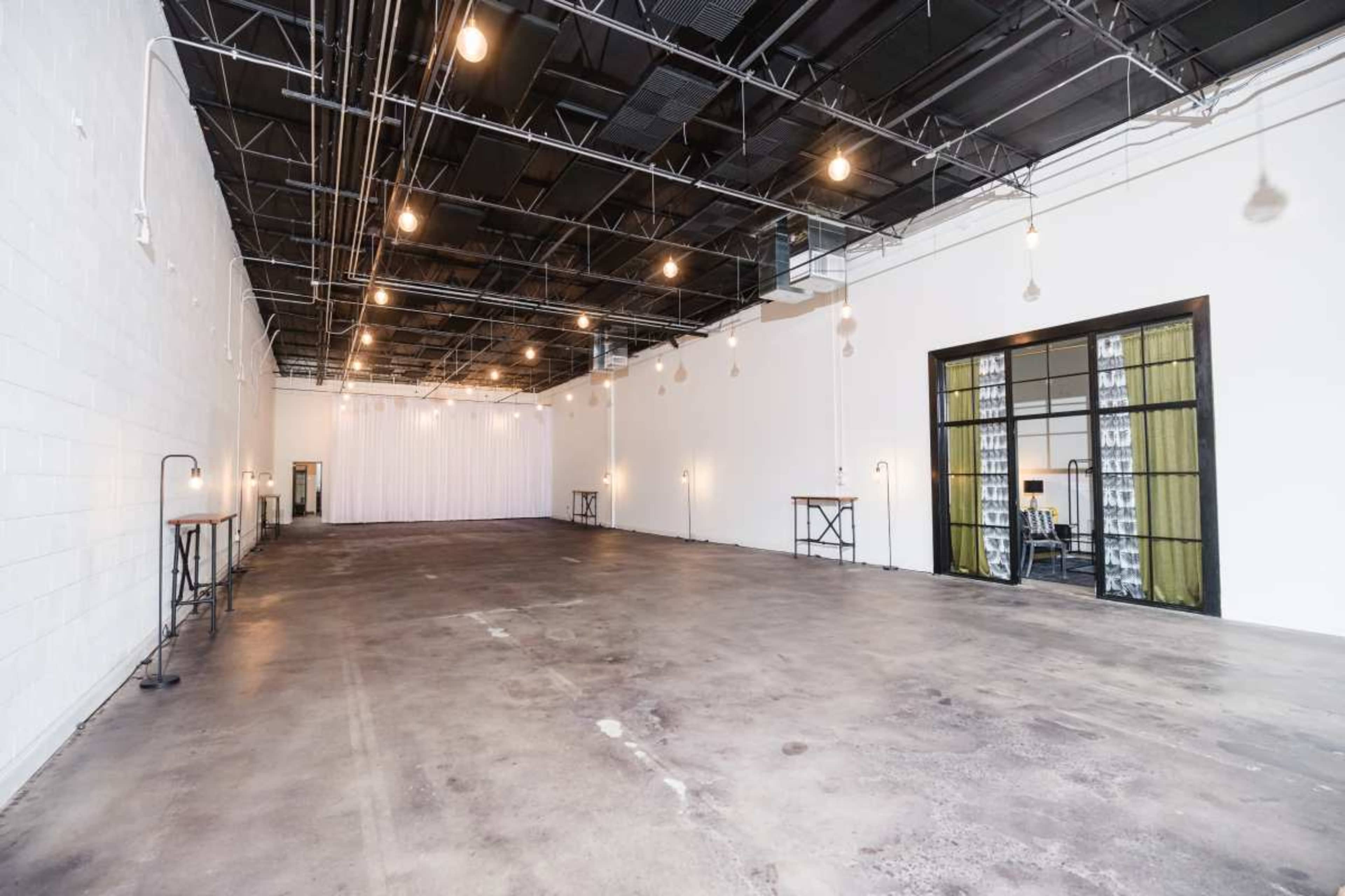 The image shows a spacious, empty interior with concrete floors, exposed ceiling beams, and several hanging light fixtures.
