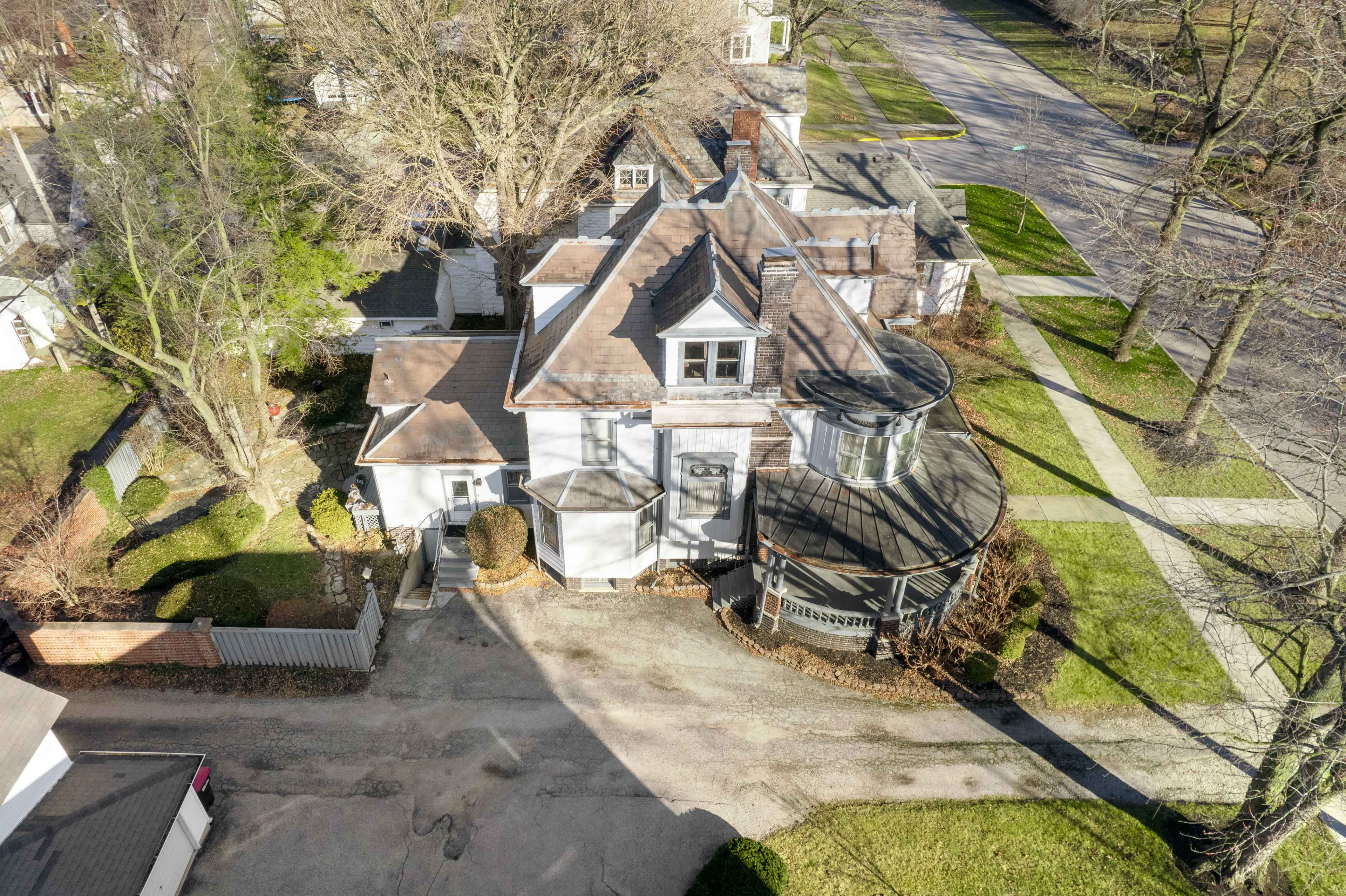 An aerial view of a house with a circular porch, surrounded by trees and a paved street.