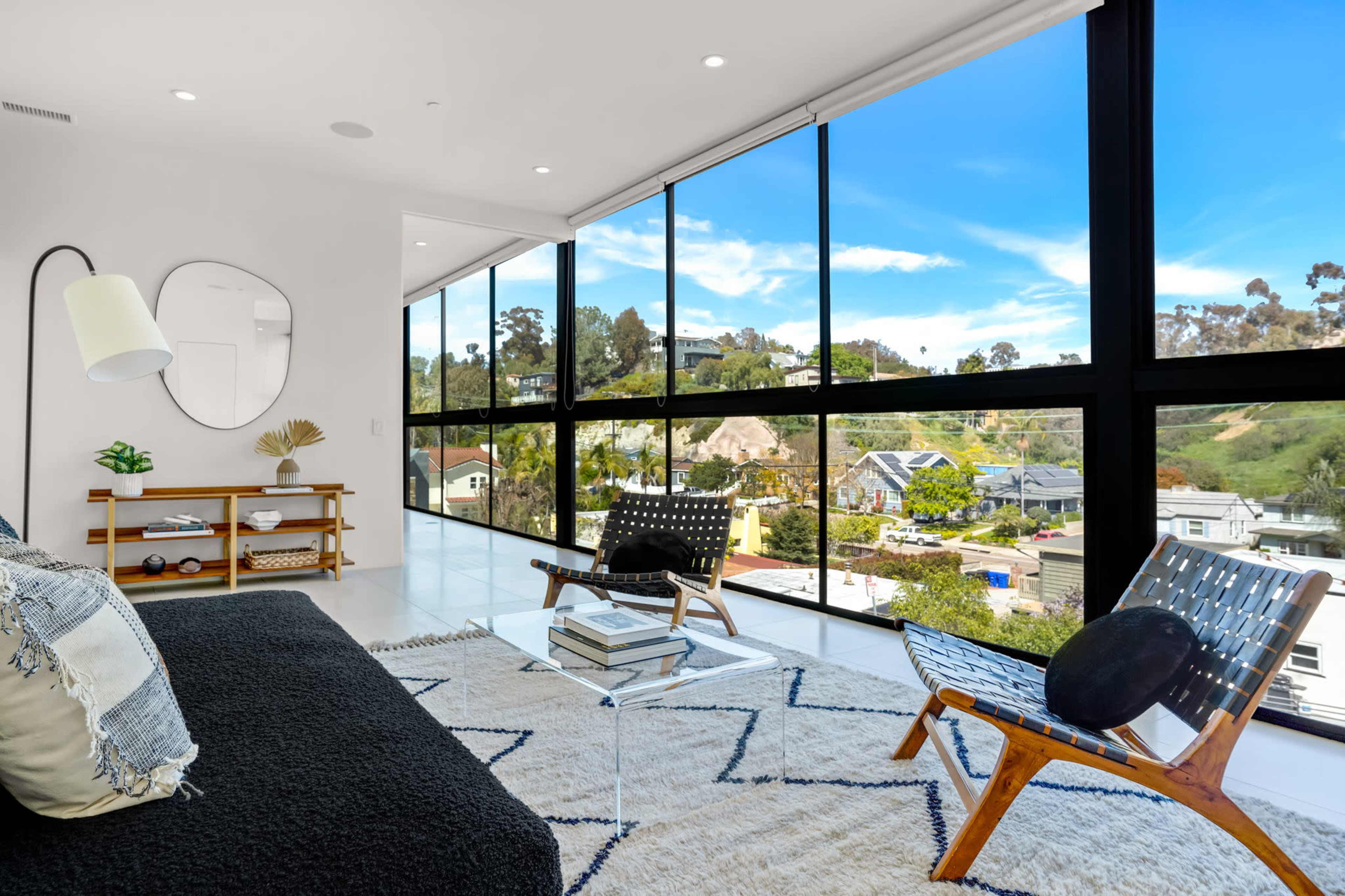 The room features large windows that provide a view of the surrounding hillside and houses.