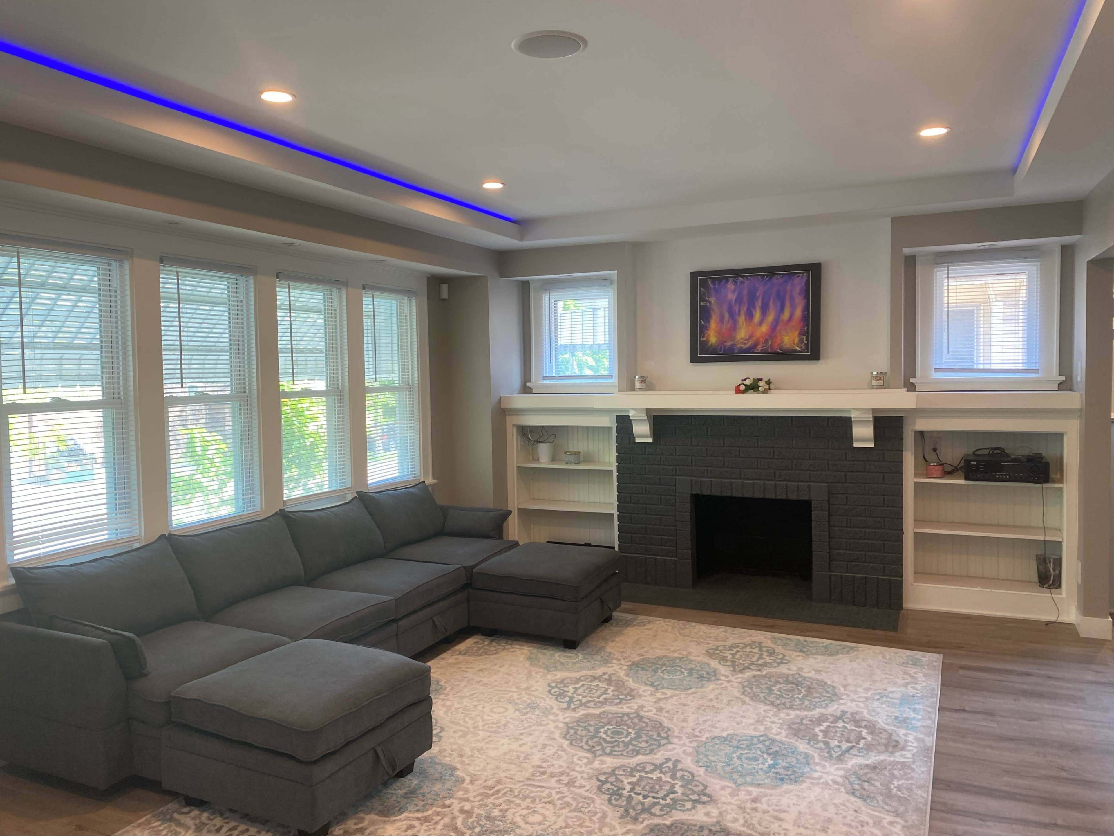 A modern living room with a gray sectional sofa, a black brick fireplace, and large windows that allow natural light to fill the space.