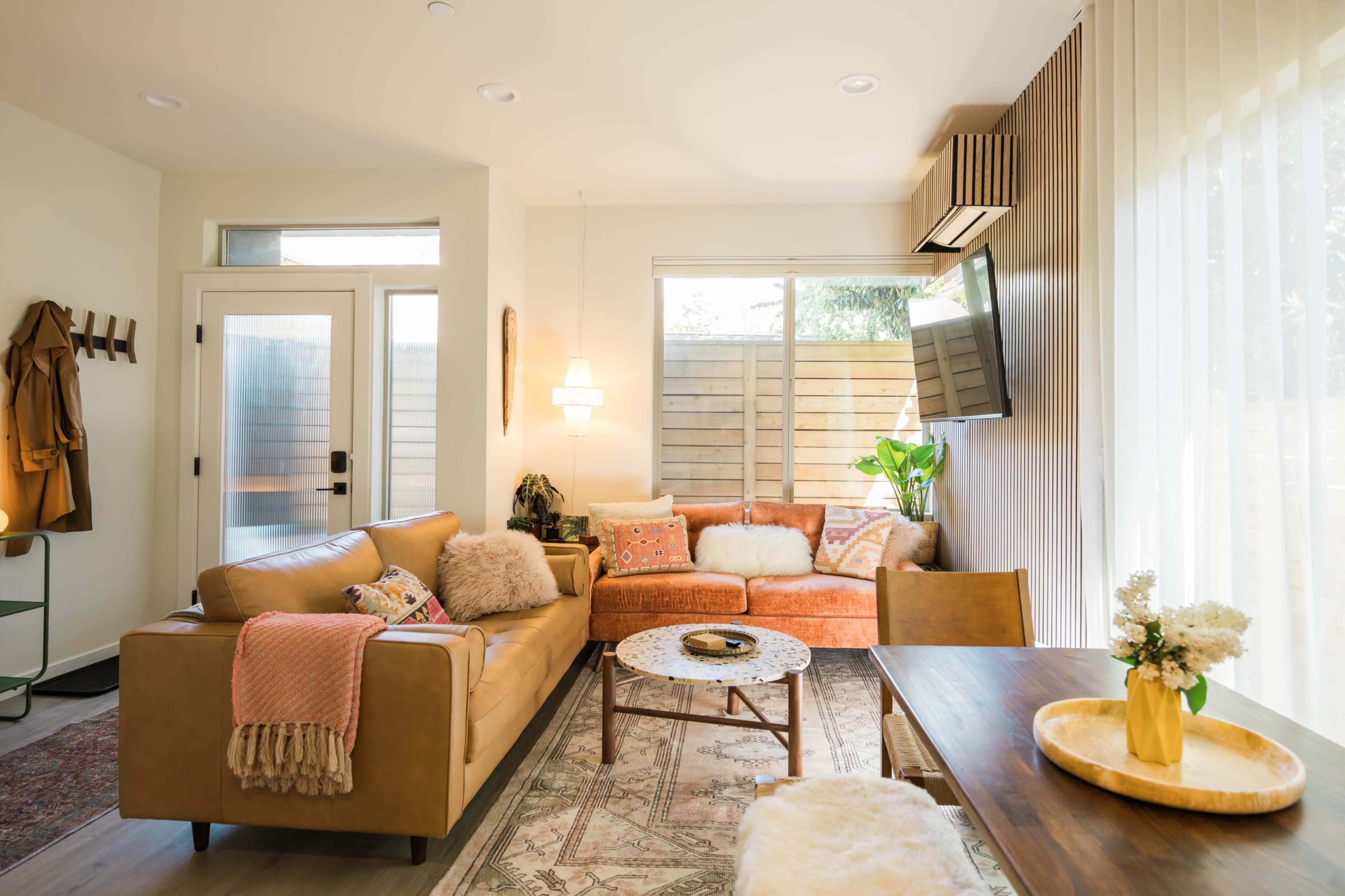 The image depicts a modern living room with a combination of leather and fabric sofas, a coffee table, and large windows allowing natural light to illuminate the space.