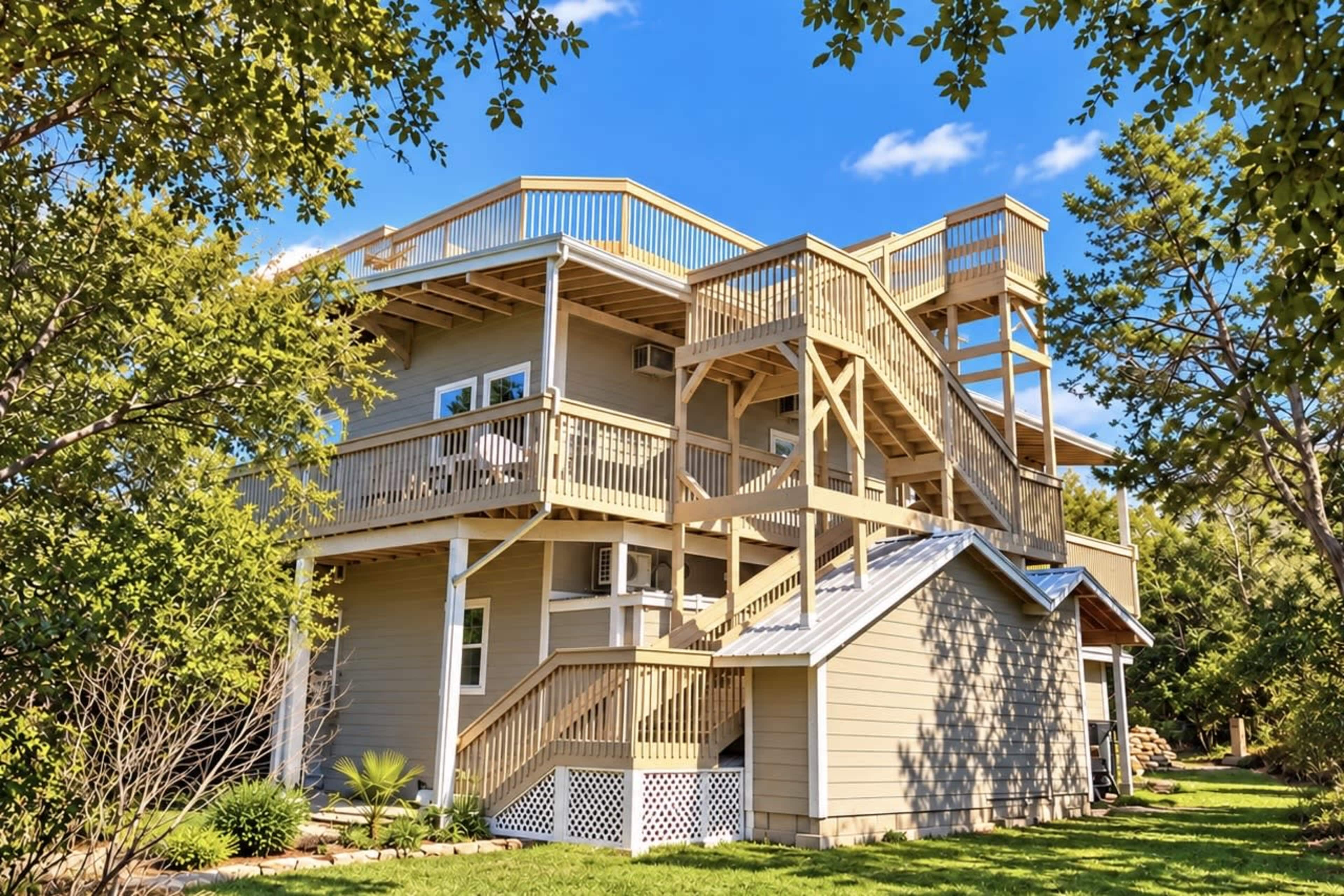 A multi-story house with wooden decks and a staircase features a landscaped yard and blue sky in the background.