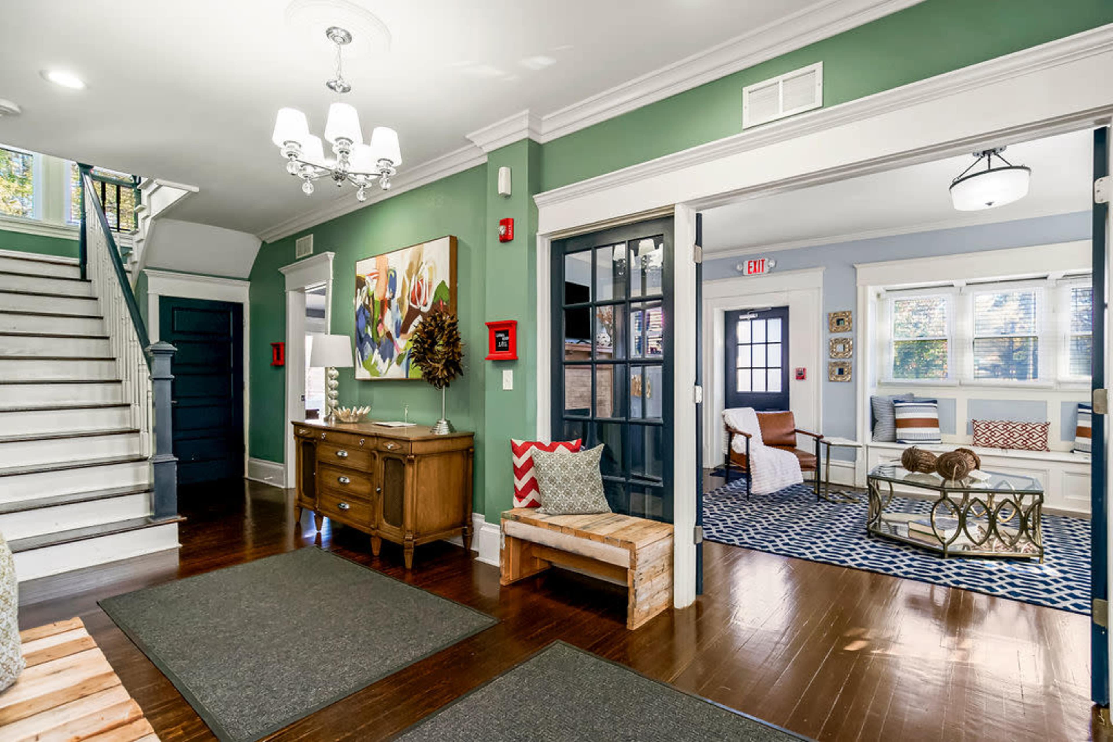 The image shows a well-lit hallway with a staircase on the left, a console table with decorative items, and a living area visible through an open door.