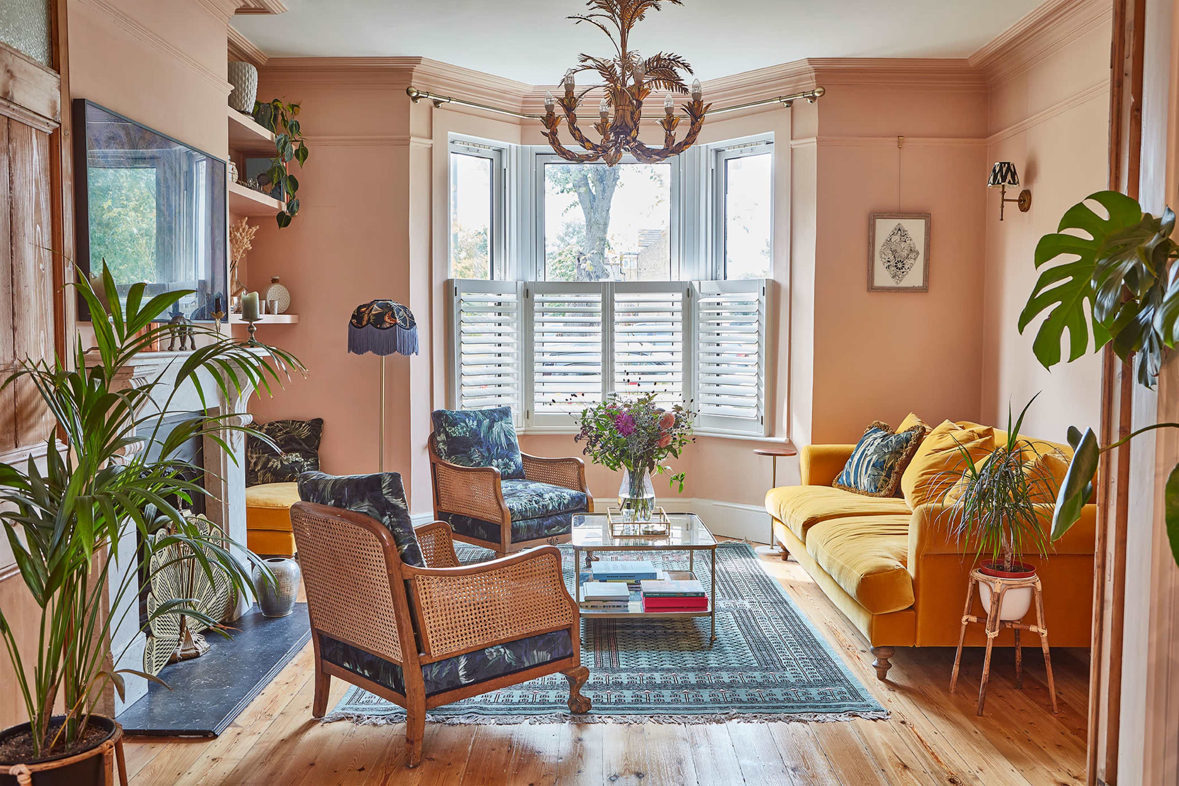 A brightly lit living room featuring a mix of seating options, including a yellow sofa, an armchair, and a coffee table surrounded by plants and natural light from large windows.