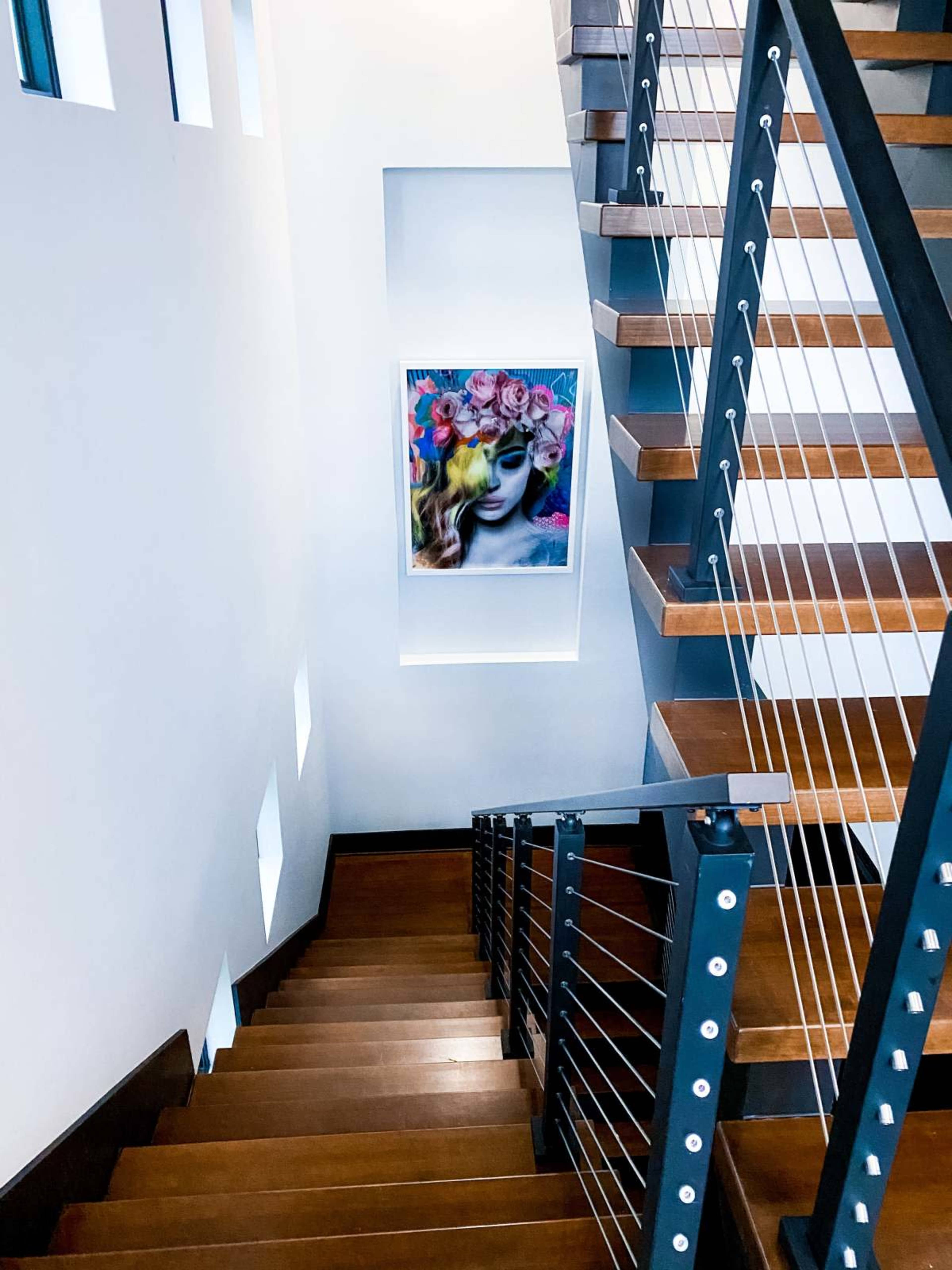 A staircase with wooden steps leads down to a landing featuring a large, framed artwork of a woman surrounded by flowers.