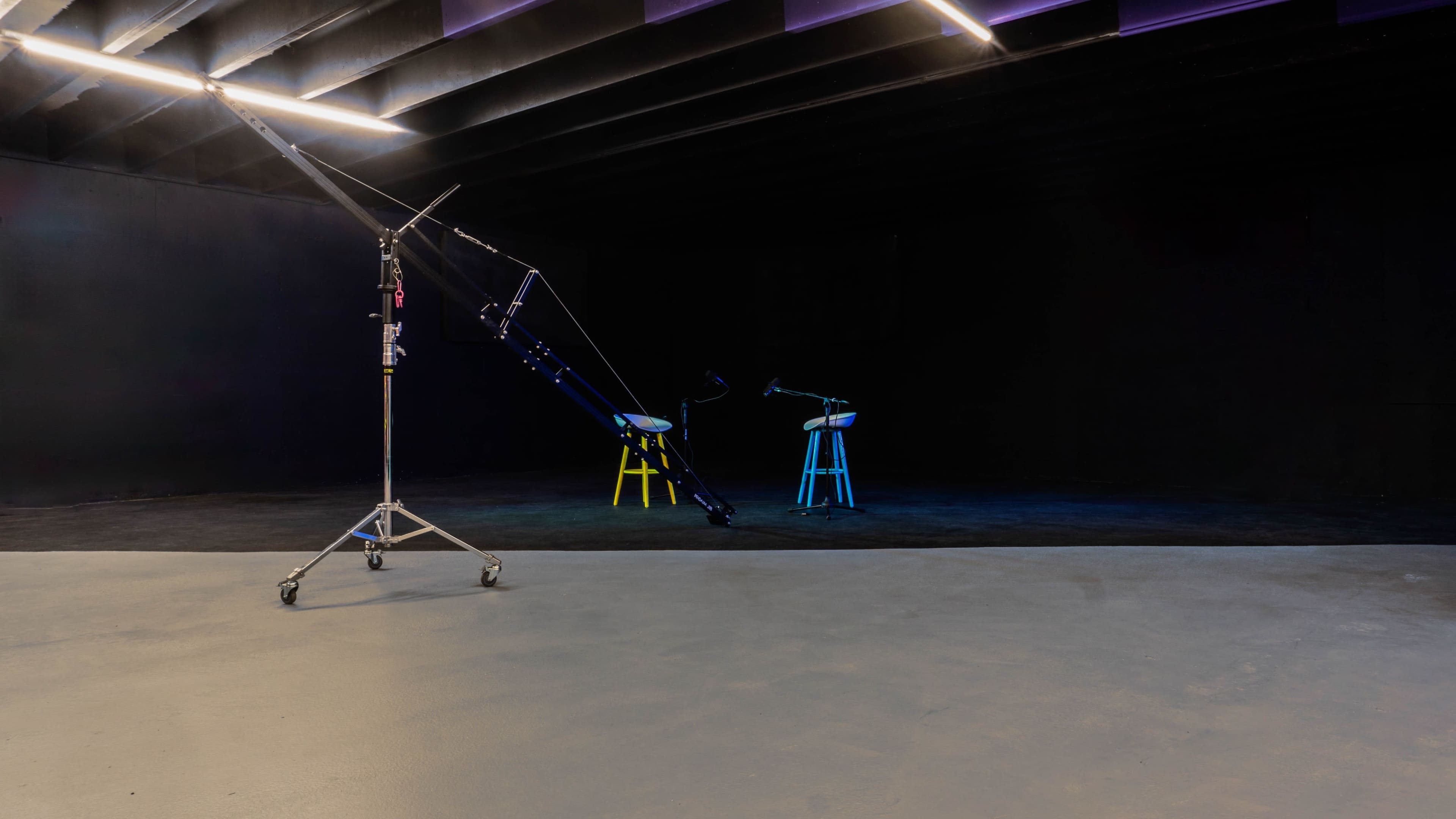 A dark studio space with two colorful stools and a boom arm set up for filming or photography.