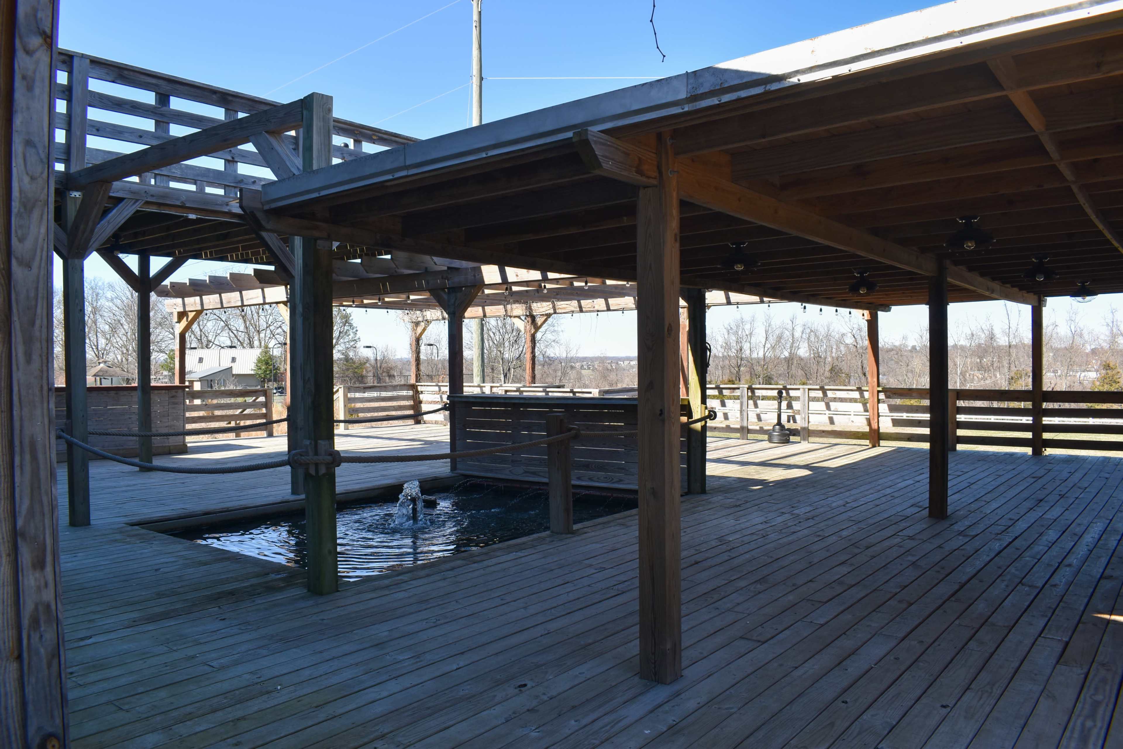 A wooden deck area with a pond in the center and a covered structure in the background.