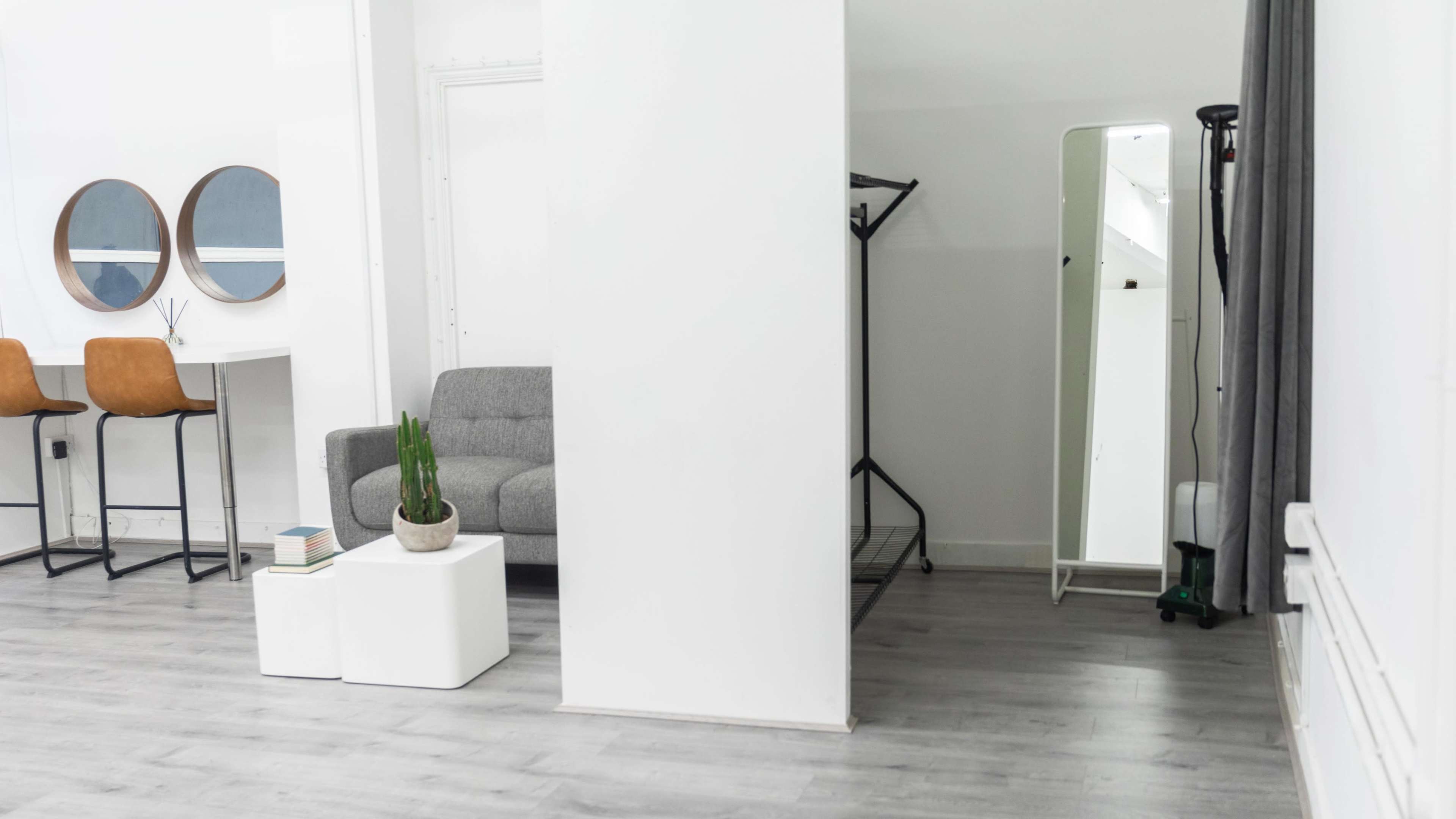 A minimalist interior space featuring a gray couch, a pair of round mirrors, a small table, and a full-length mirror against a wall.