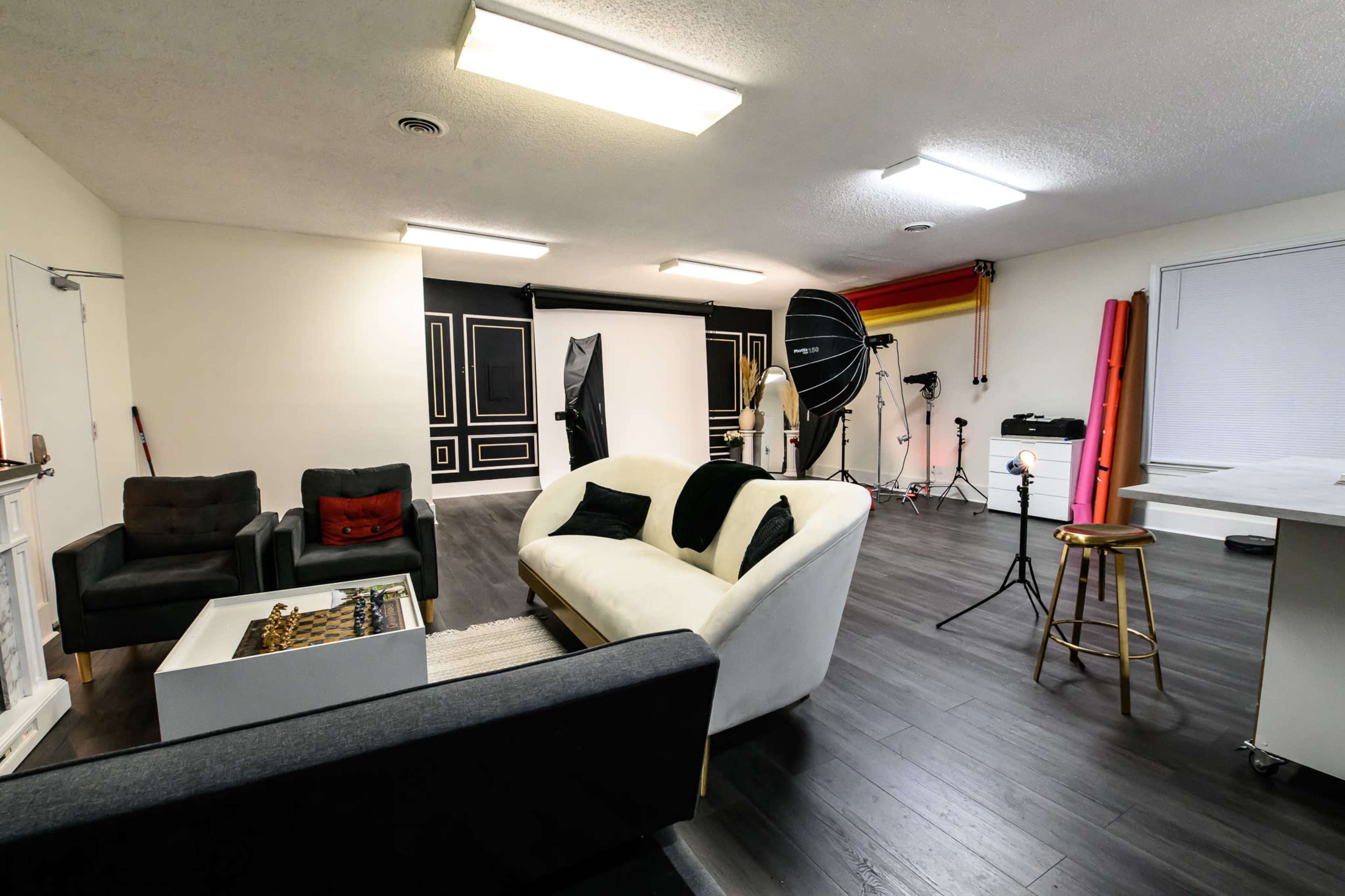 A studio space featuring a white sofa, dark seating, a photography backdrop, lighting equipment, and various props arranged for a photoshoot.