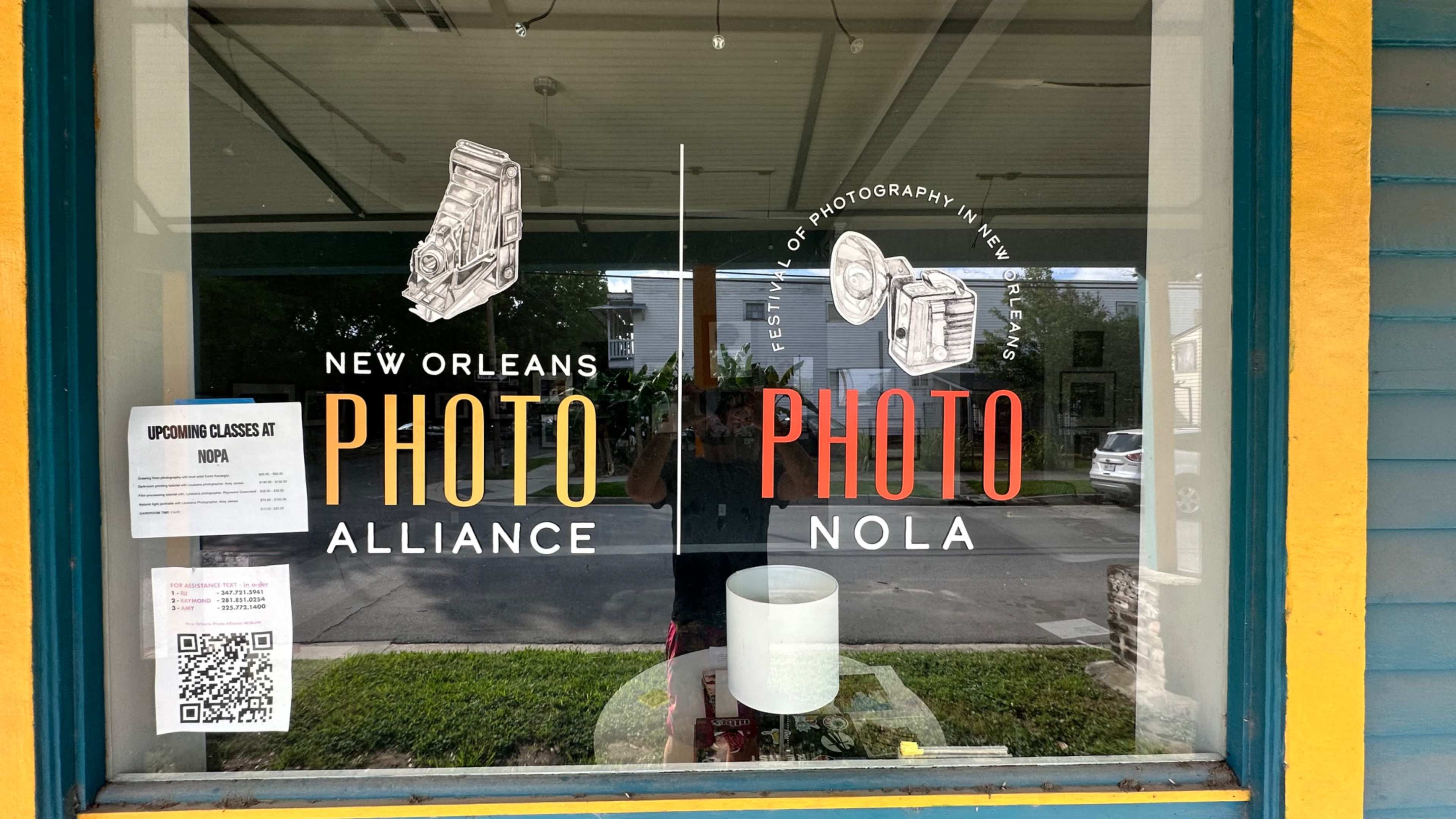 The window display features the names "New Orleans Photo Alliance" and "Photo NOLA" alongside illustrations of a camera and a photography-related device.
