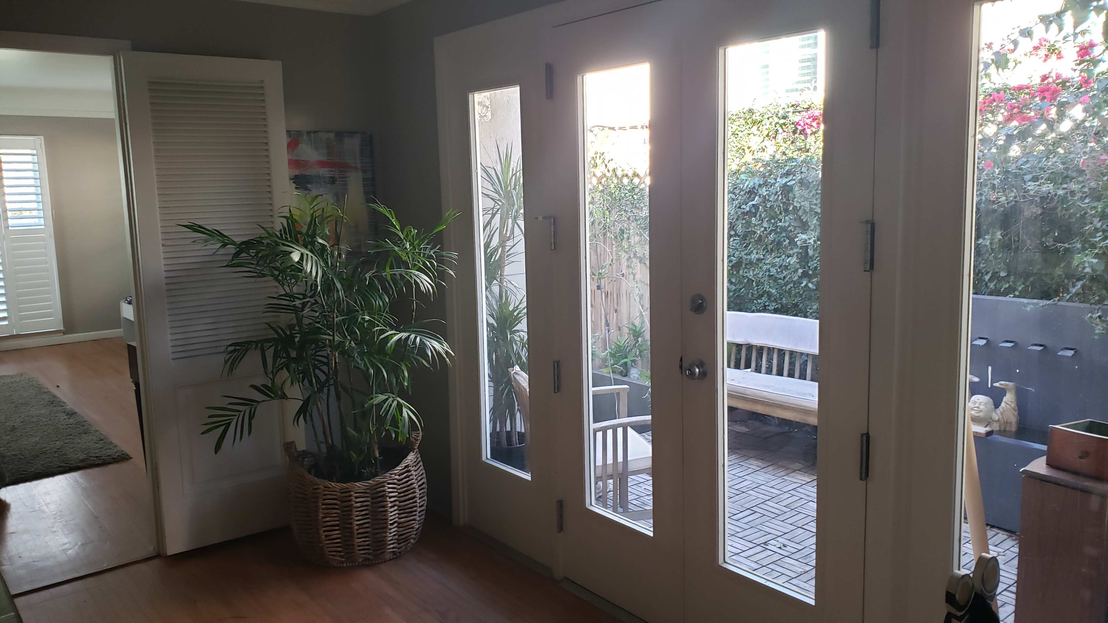 A well-lit entrance with glass-paneled double doors leading to a small outdoor seating area surrounded by greenery.