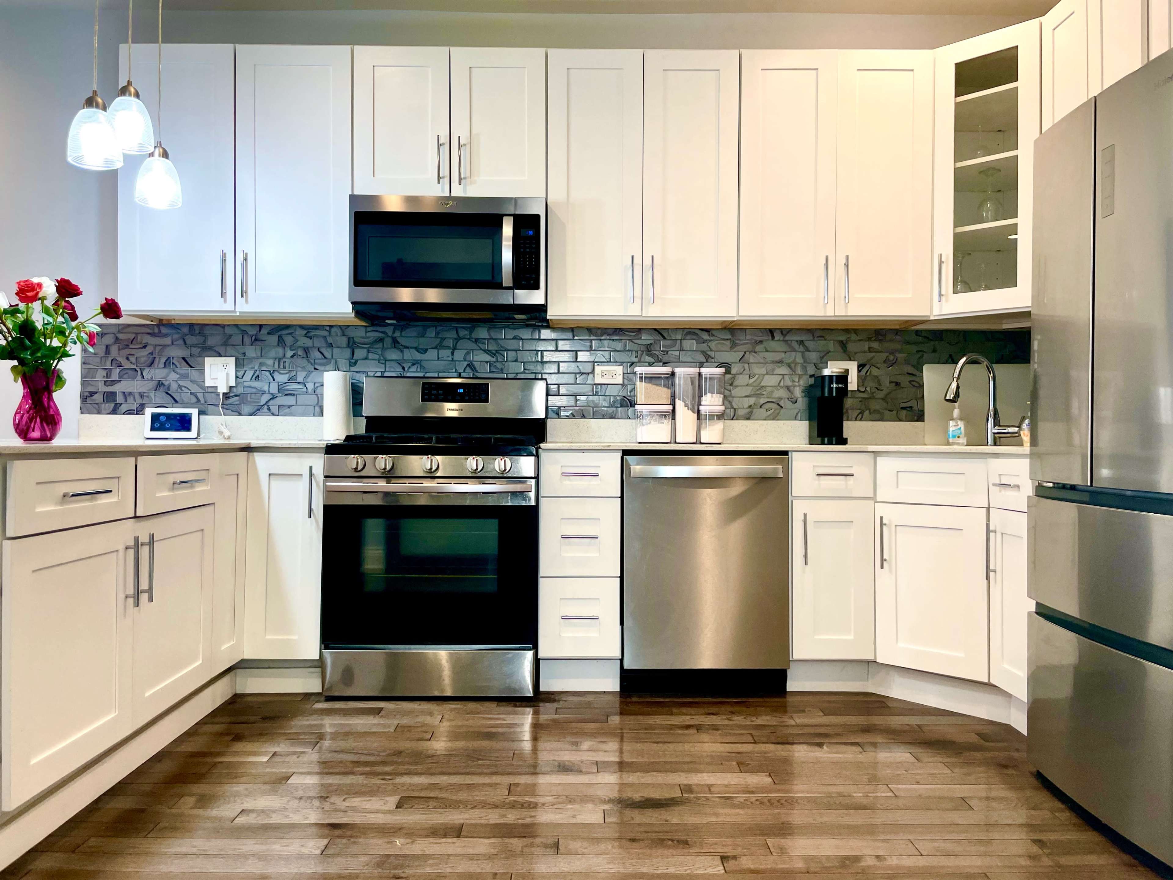 A modern kitchen features white cabinets, stainless steel appliances, and a marble backsplash, complemented by a vase of red roses on the counter.
