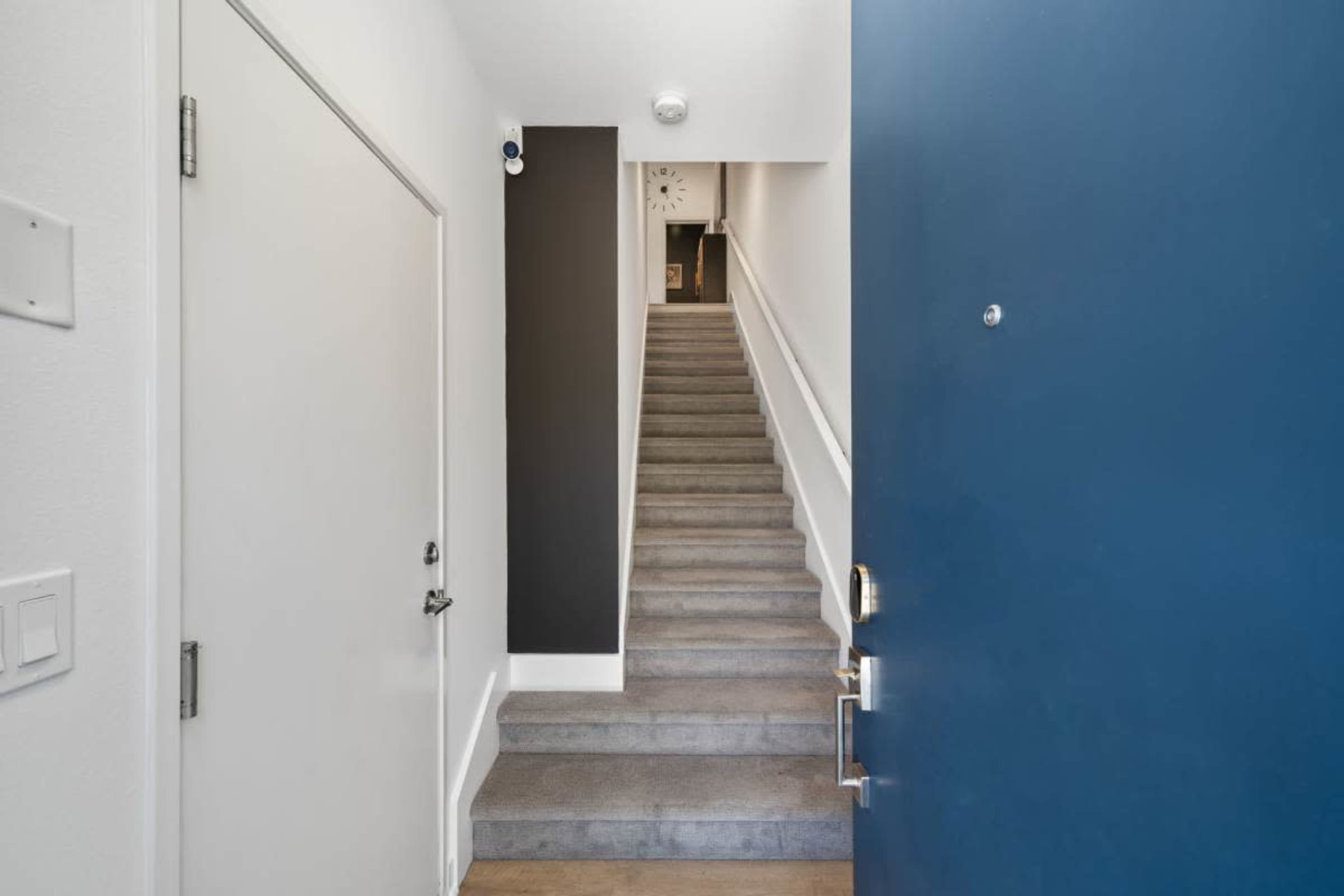 A view of a hallway with a blue front door and a staircase leading upward.
