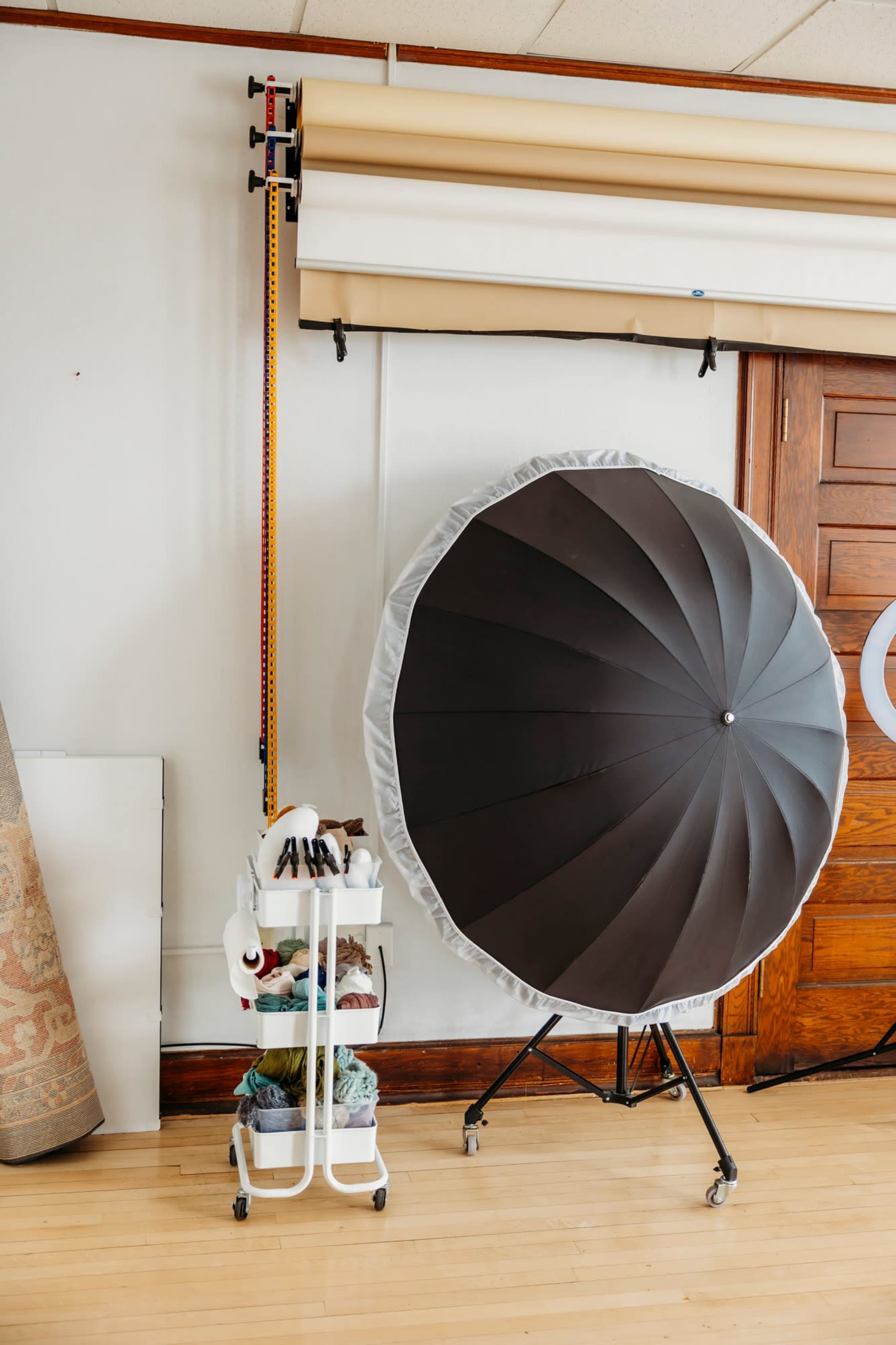 A photography studio setup featuring a large softbox on a stand next to a mobile cart filled with various photography accessories.