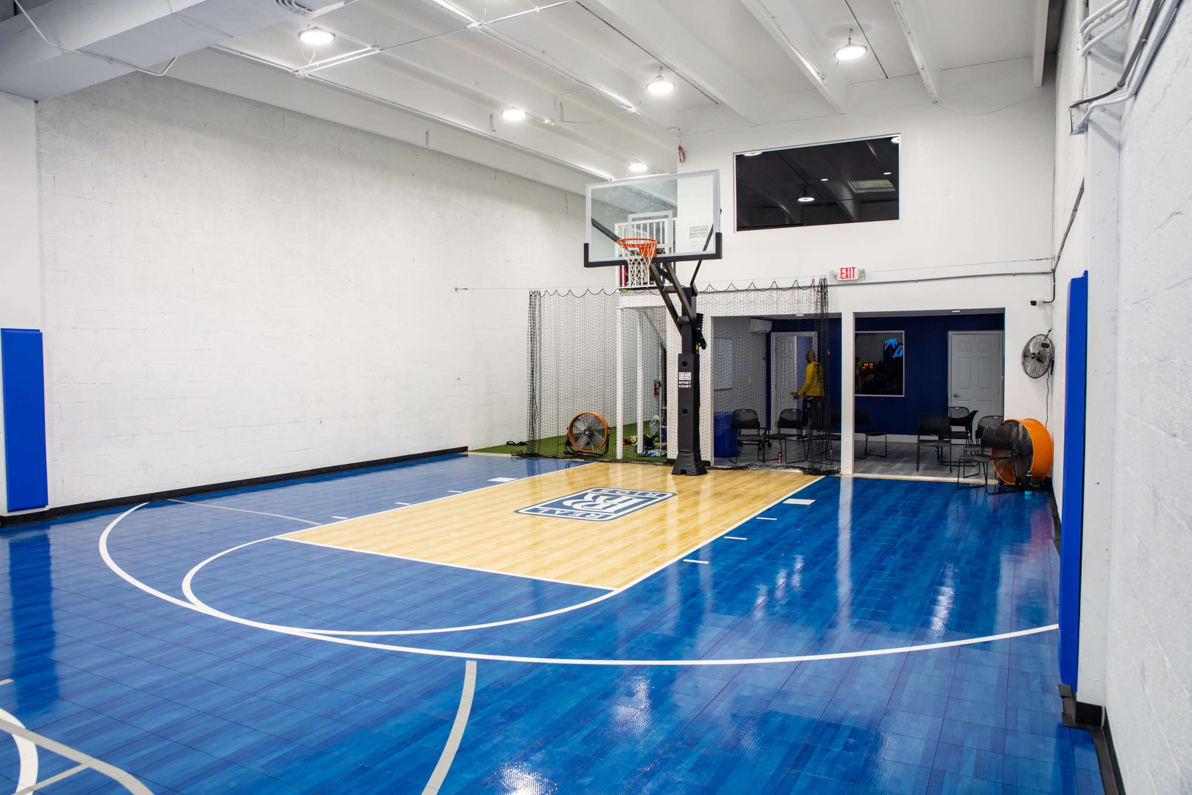 A basketball court with a blue wooden floor, a hoop, and some equipment in the background.