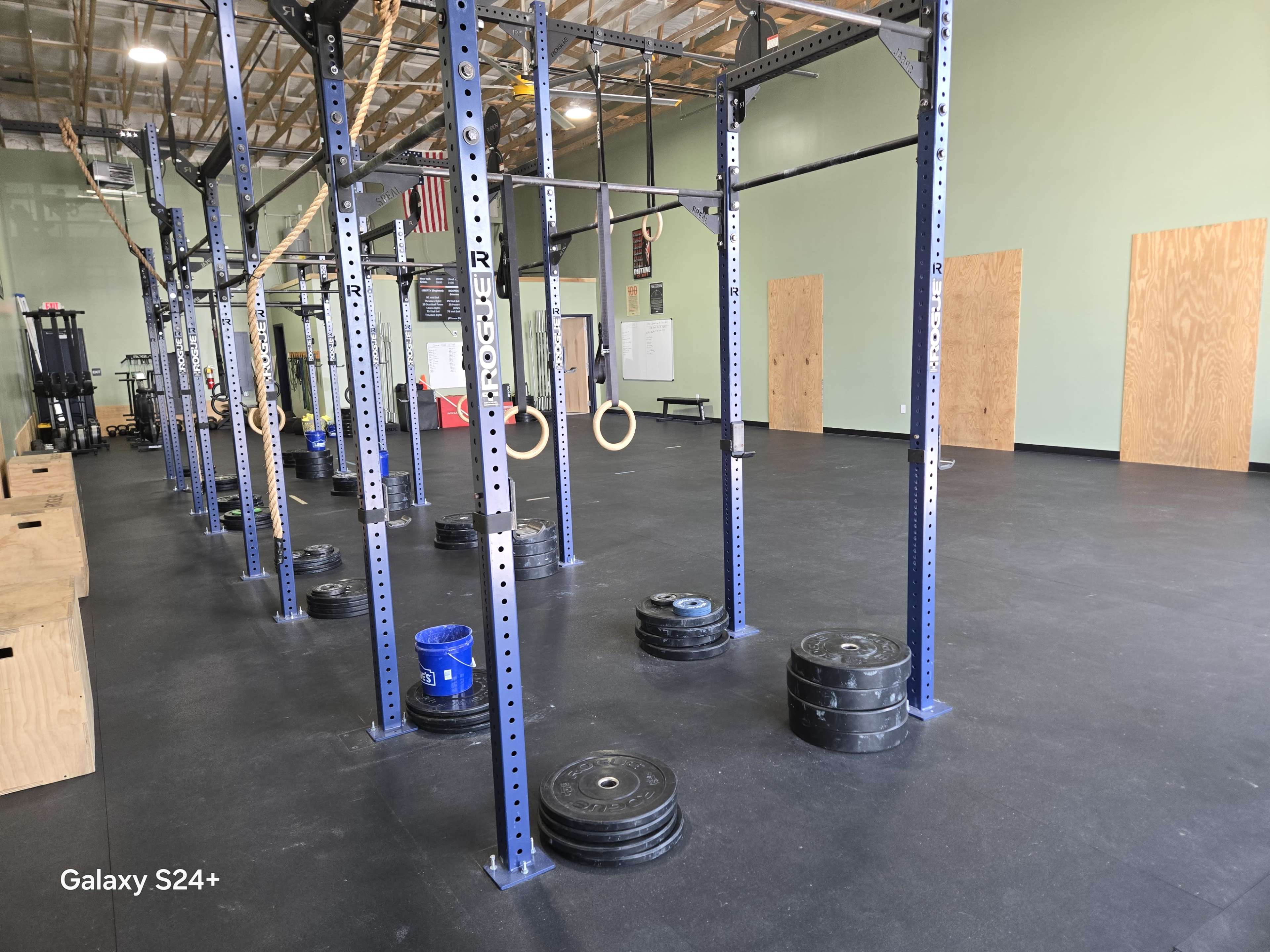 The image shows a gym interior featuring weightlifting equipment, including barbells with weights and wooden panels on the walls.