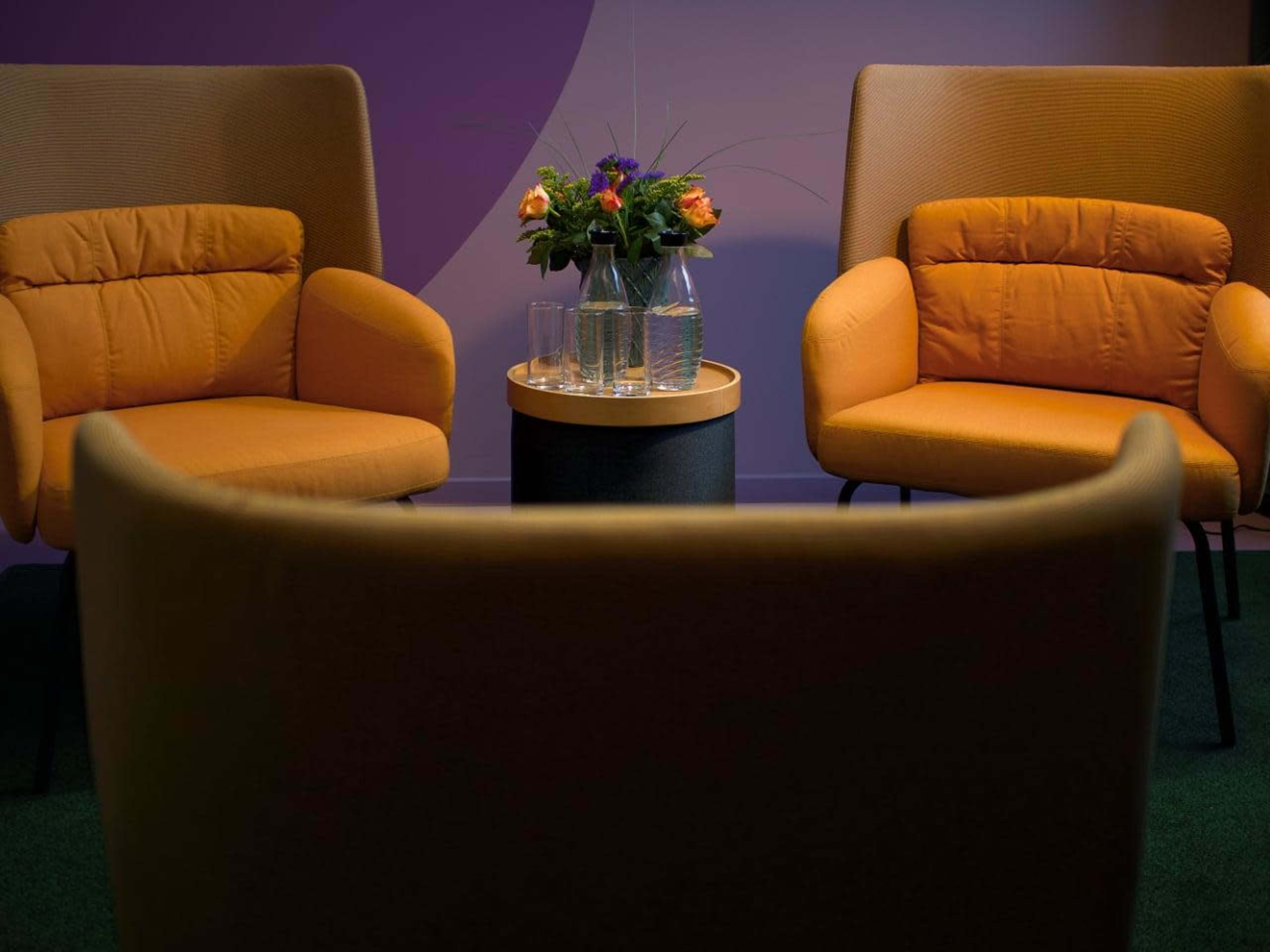 Two yellow armchairs are positioned facing a small table adorned with a vase of flowers, set against a purple wall.