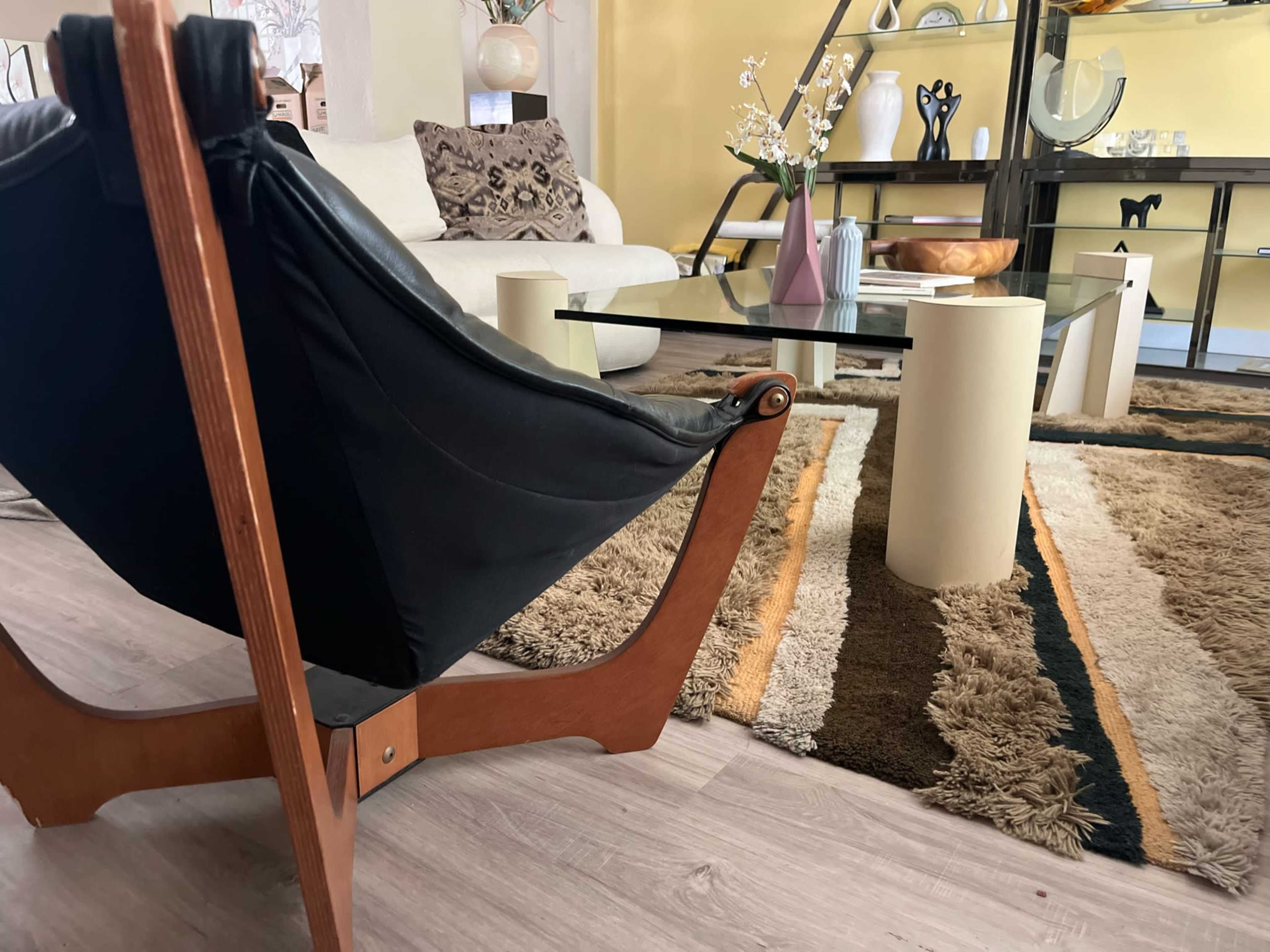 A modern living room with a black chair, a glass coffee table, and a patterned rug.
