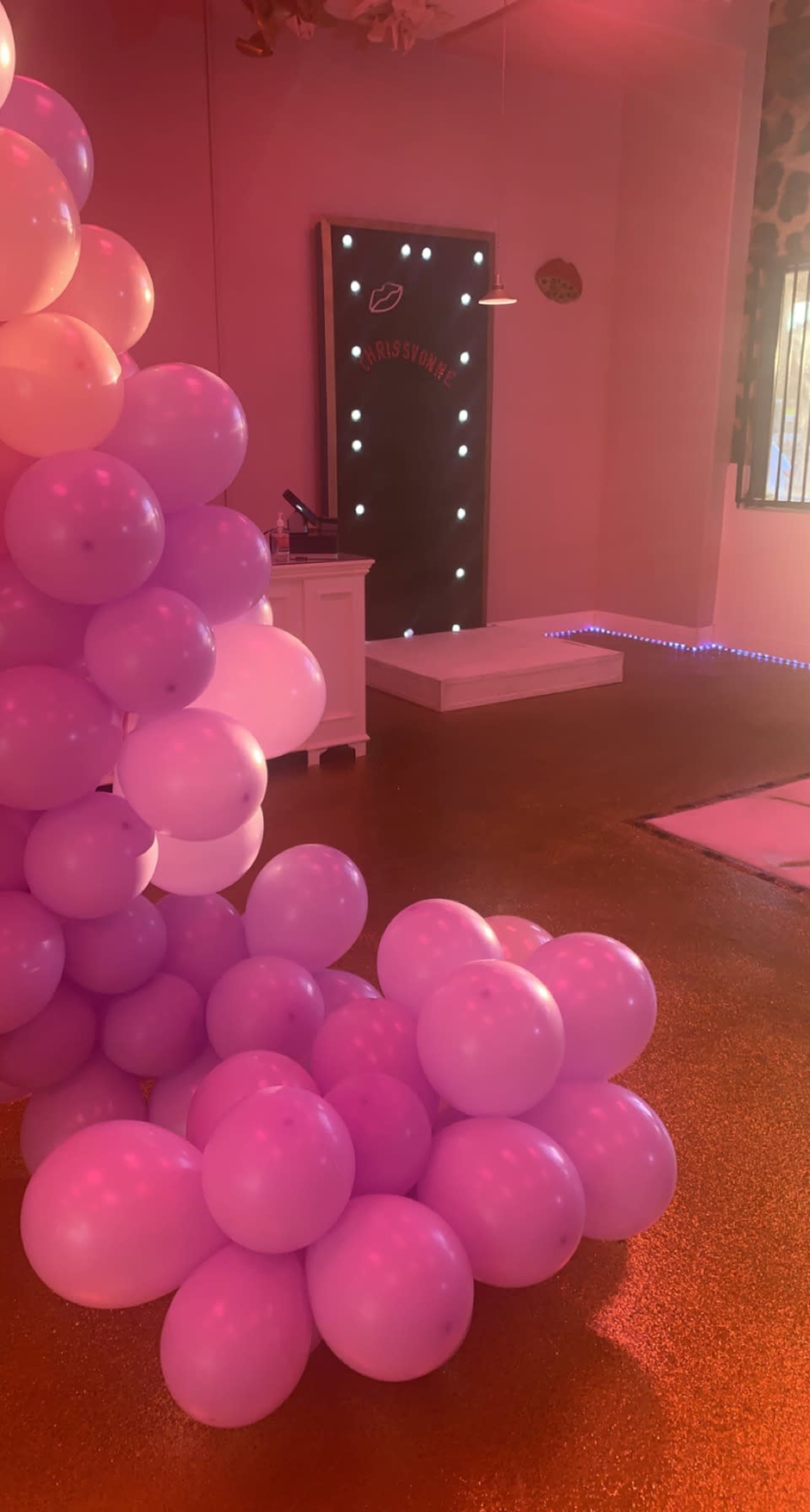The scene features a playful interior decorated with clusters of purple balloons, a lighted backdrop, and a small stage area.